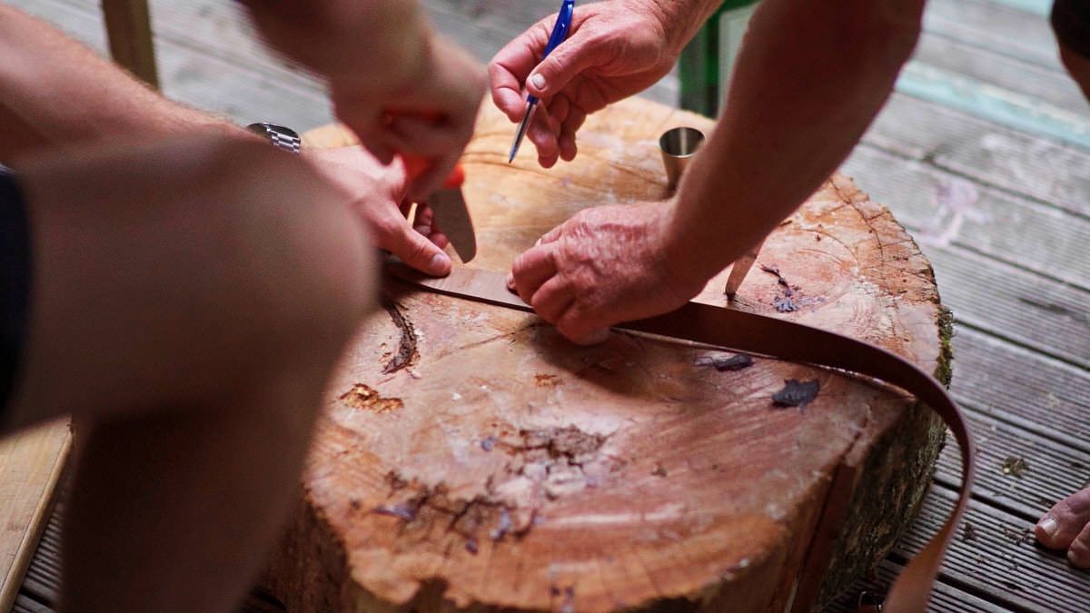 Two people measuring and marking a freshly cut wood log cross-section with a ruler and pencil on a wooden deck.