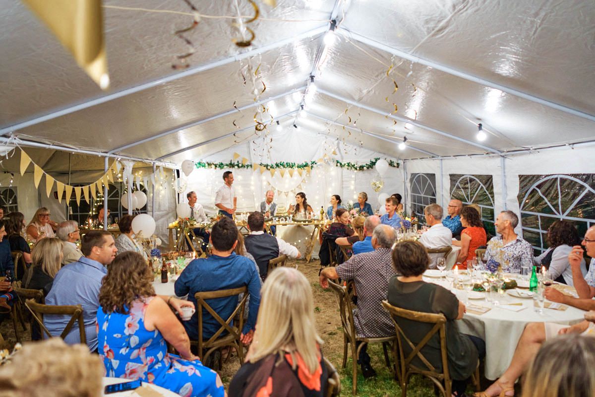 Guests seated at round tables under a white tent during an elegant outdoor wedding reception dinner.