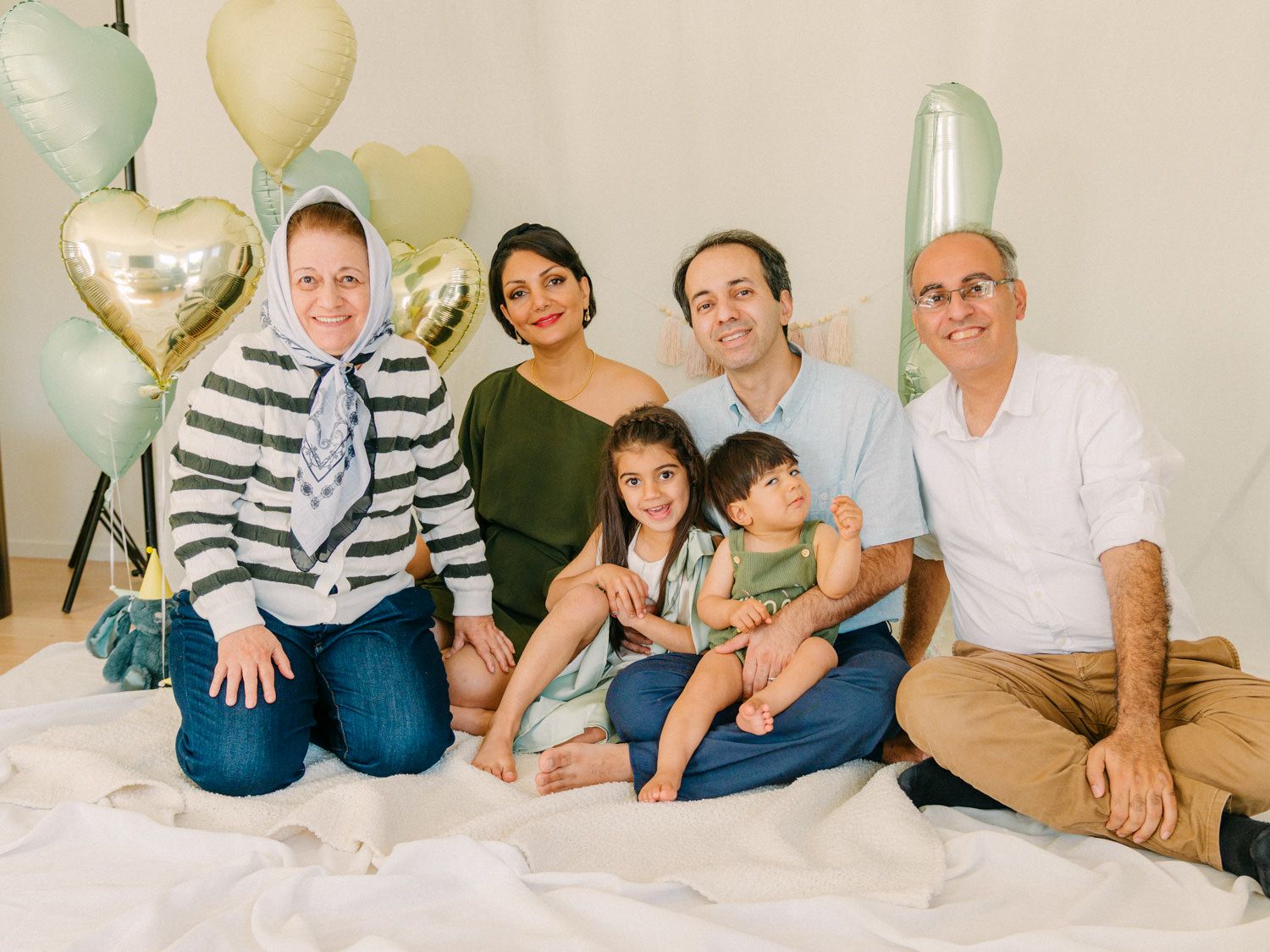 Family of six poses together with heart-shaped balloons in a bright studio setting for a celebratory photo session.