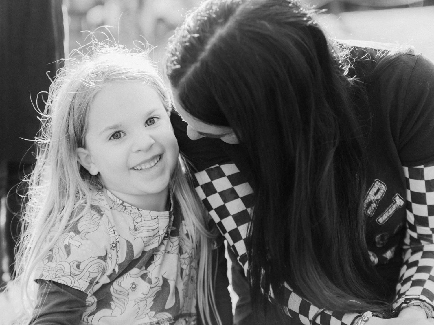 Black and white close-up of a smiling young girl with a woman leaning in beside her.
