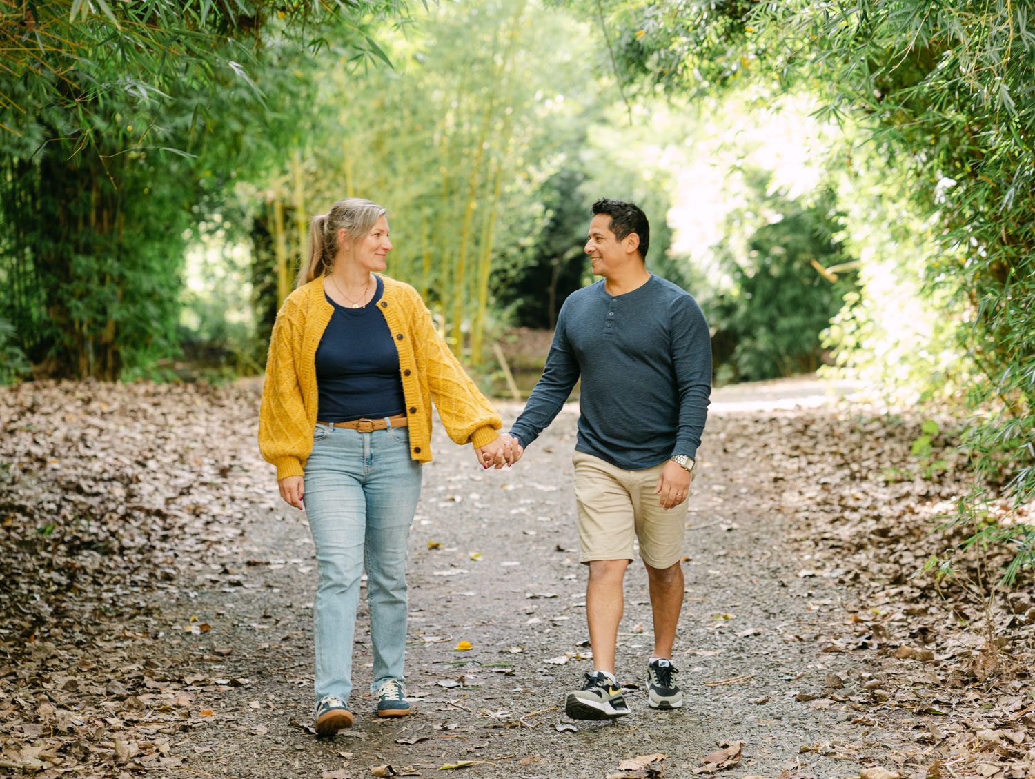 Couple holding hands walking on a leafy path surrounded by lush green bamboo trees.