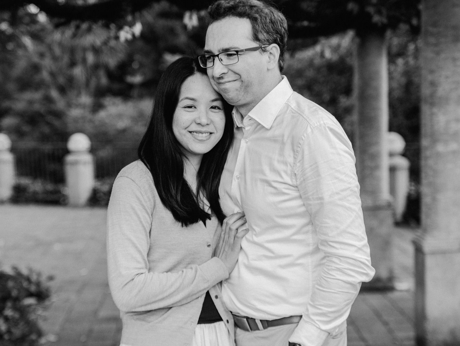 Black and white photo of a smiling couple embracing outdoors in a park setting.
