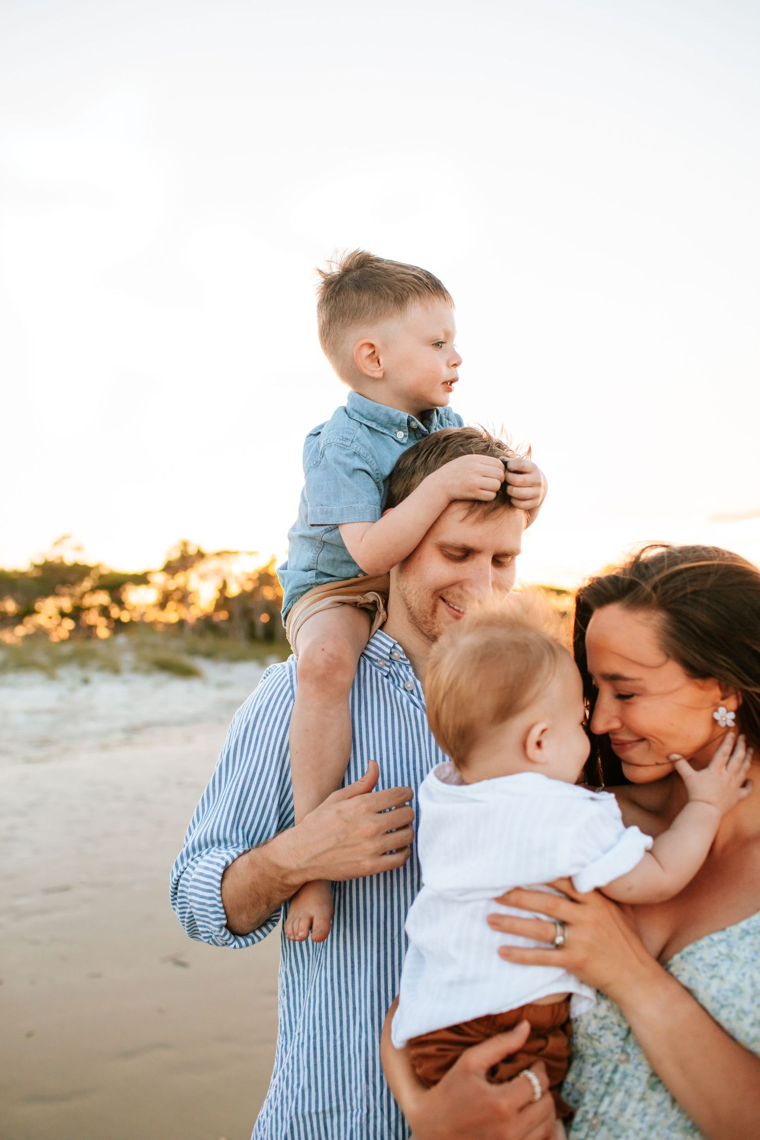 Family of four enjoying a sunset beach moment with toddler on dad's shoulders.