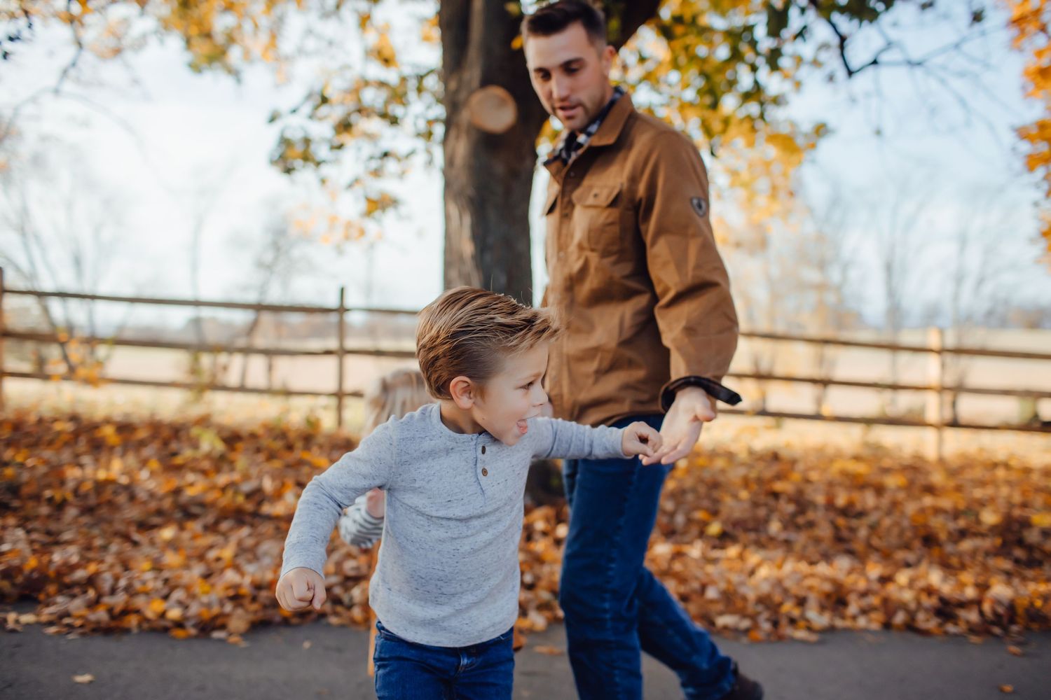 Father and young son walking hand in hand on a path during fall season.