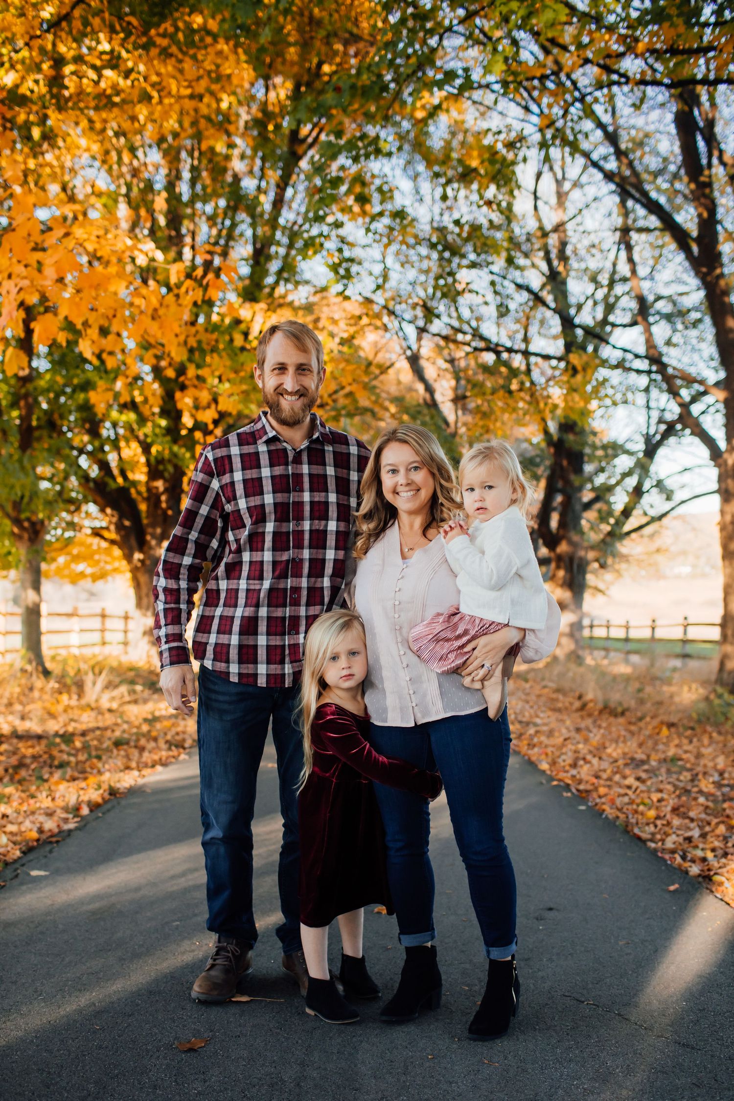 Family of four posing on a tree-lined path during autumn foliage season.