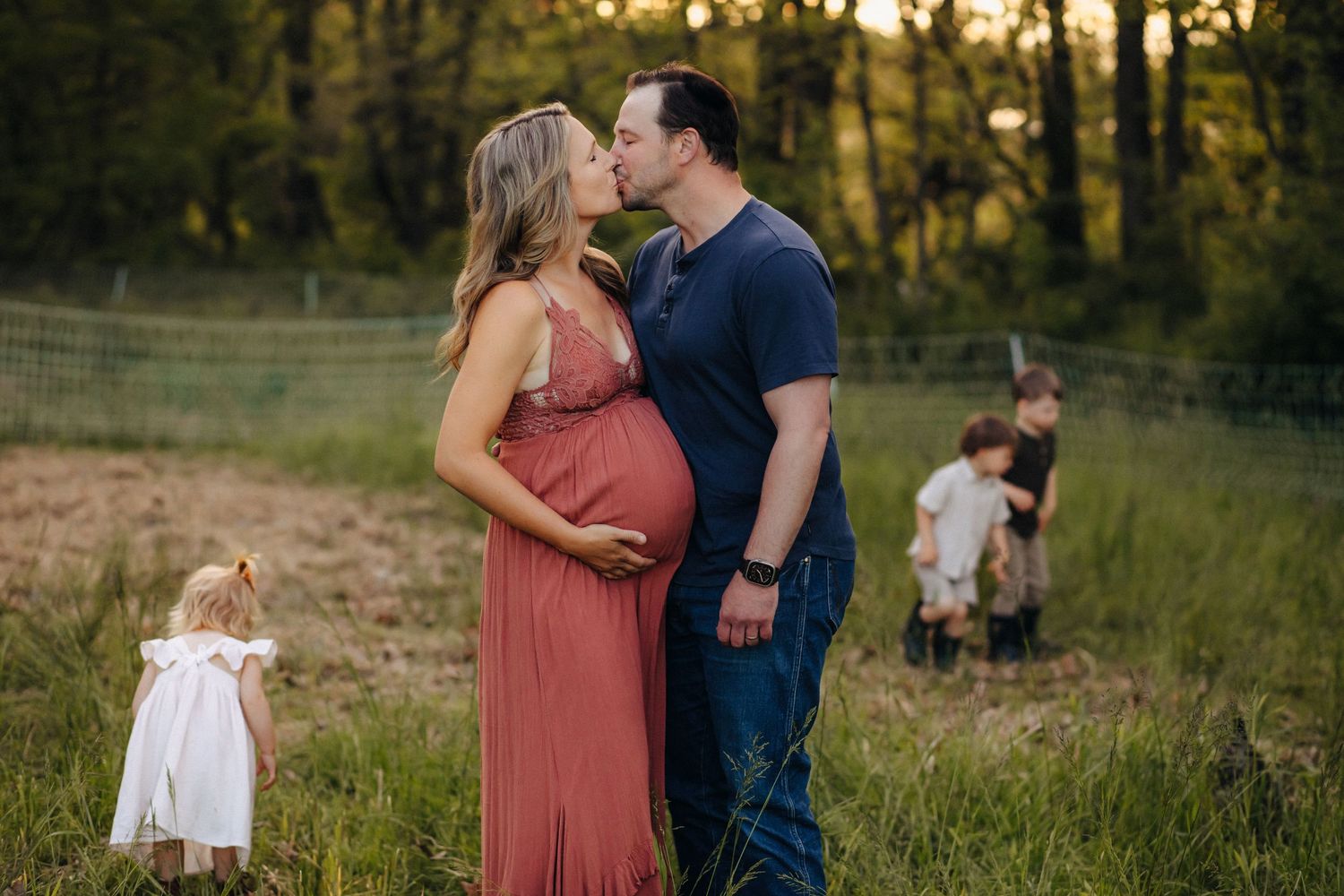 Couple sharing a kiss in a field at sunset during a maternity photo session.