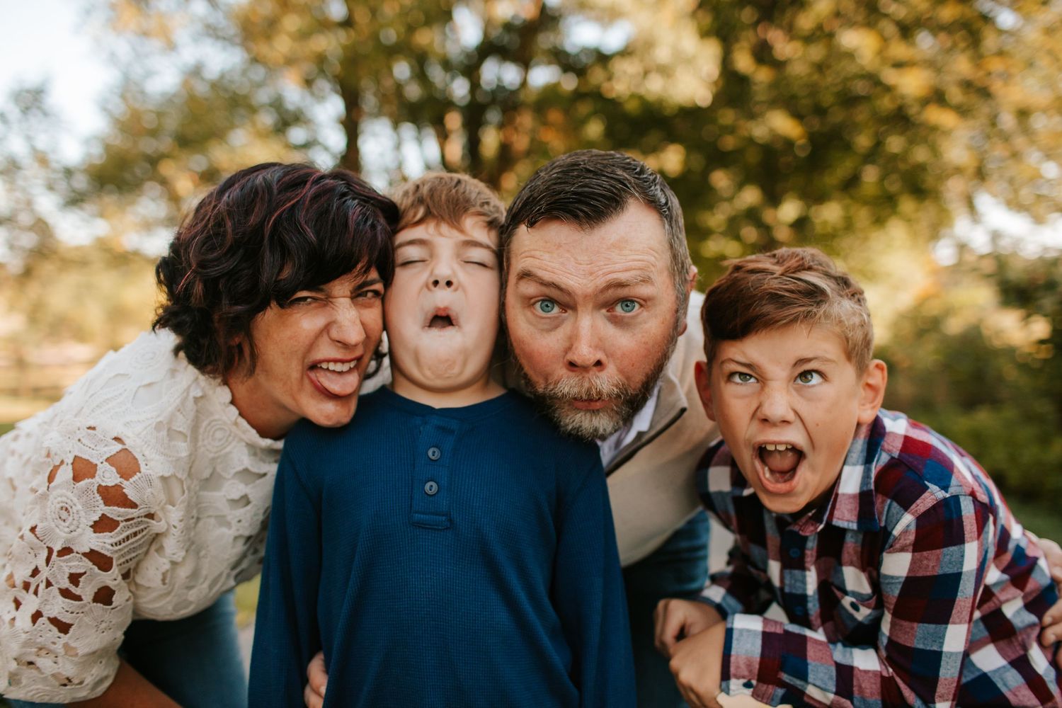 Fun family portrait of parents and two boys making silly faces outdoors.