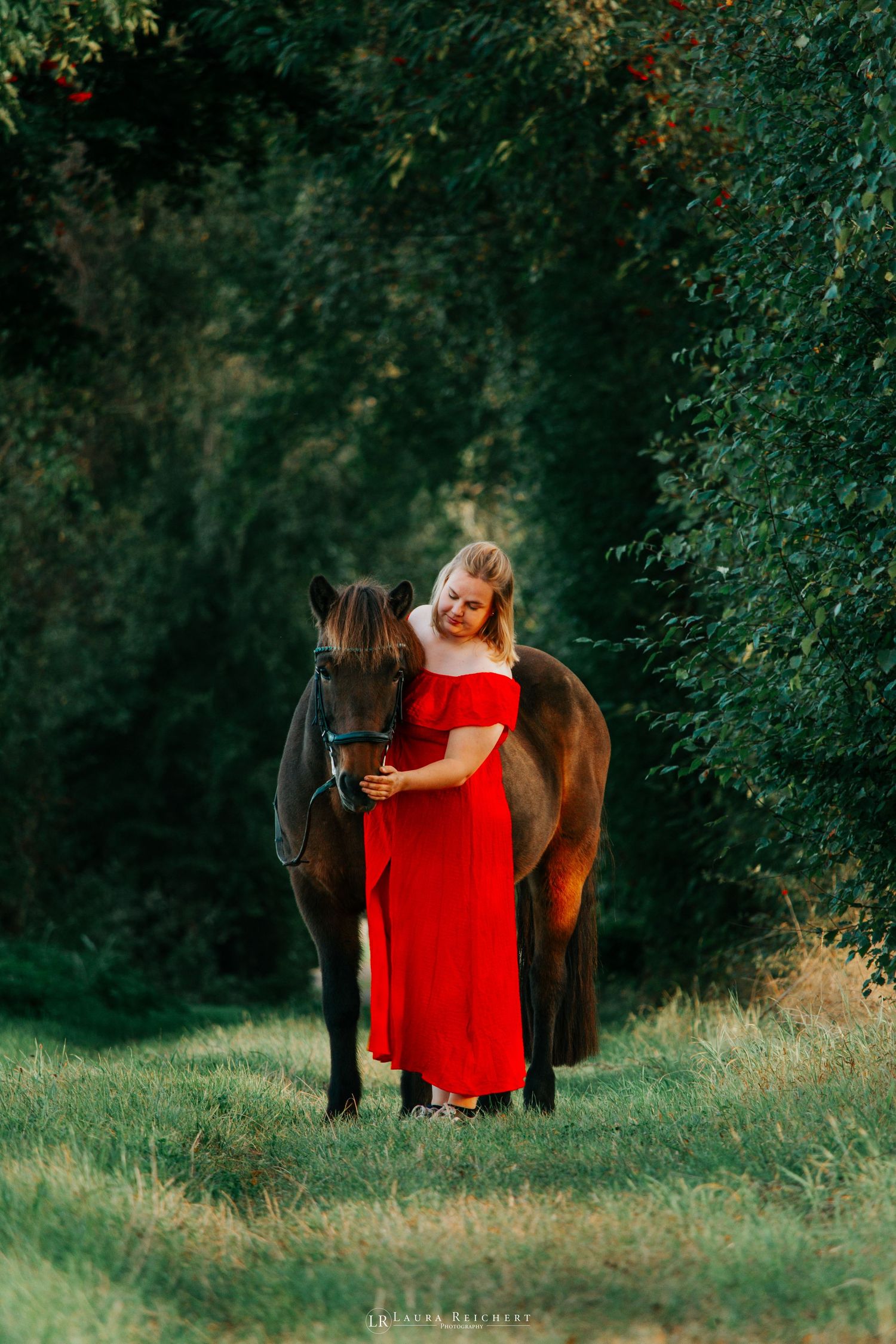 Mädchen mit ihrem Pony im Wald im roten Kleid im Sommer.
