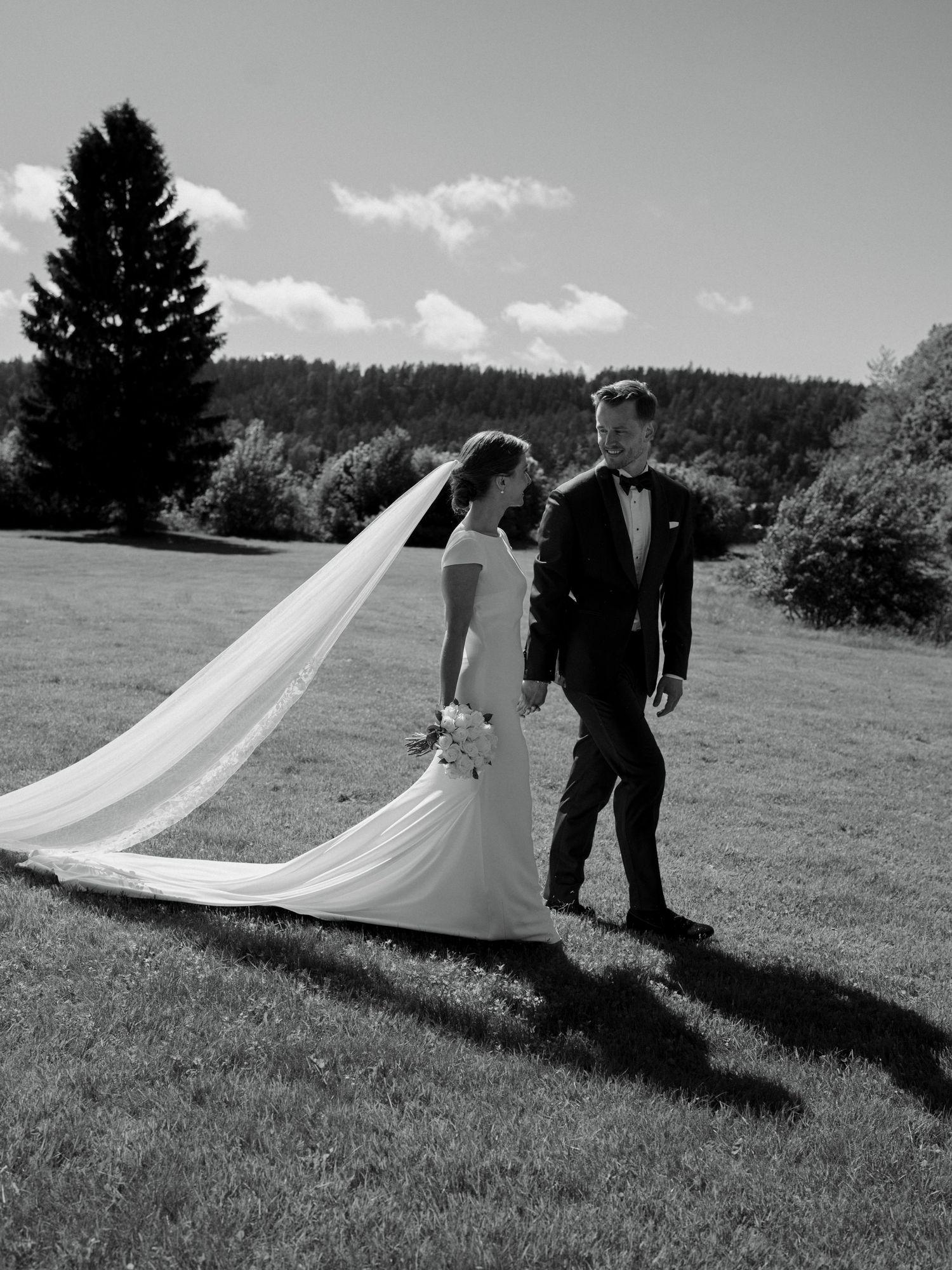Black and white photo of bride and groom walking on green lawn.