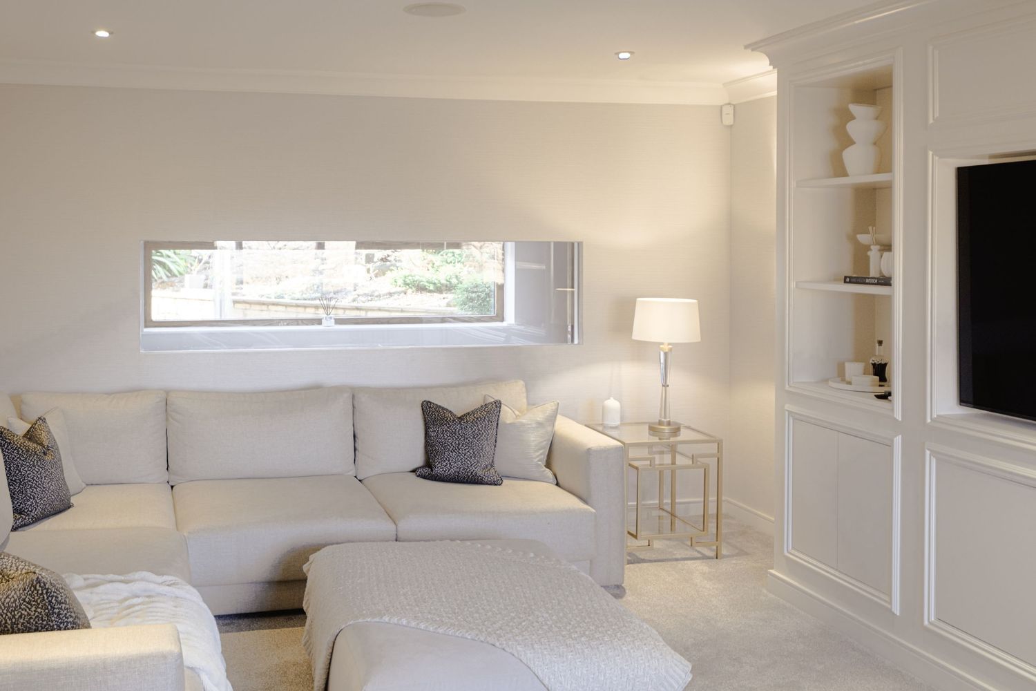 Bright modern living room featuring white leather  sofas, colour coordinated book shelves and a wall mounted television
