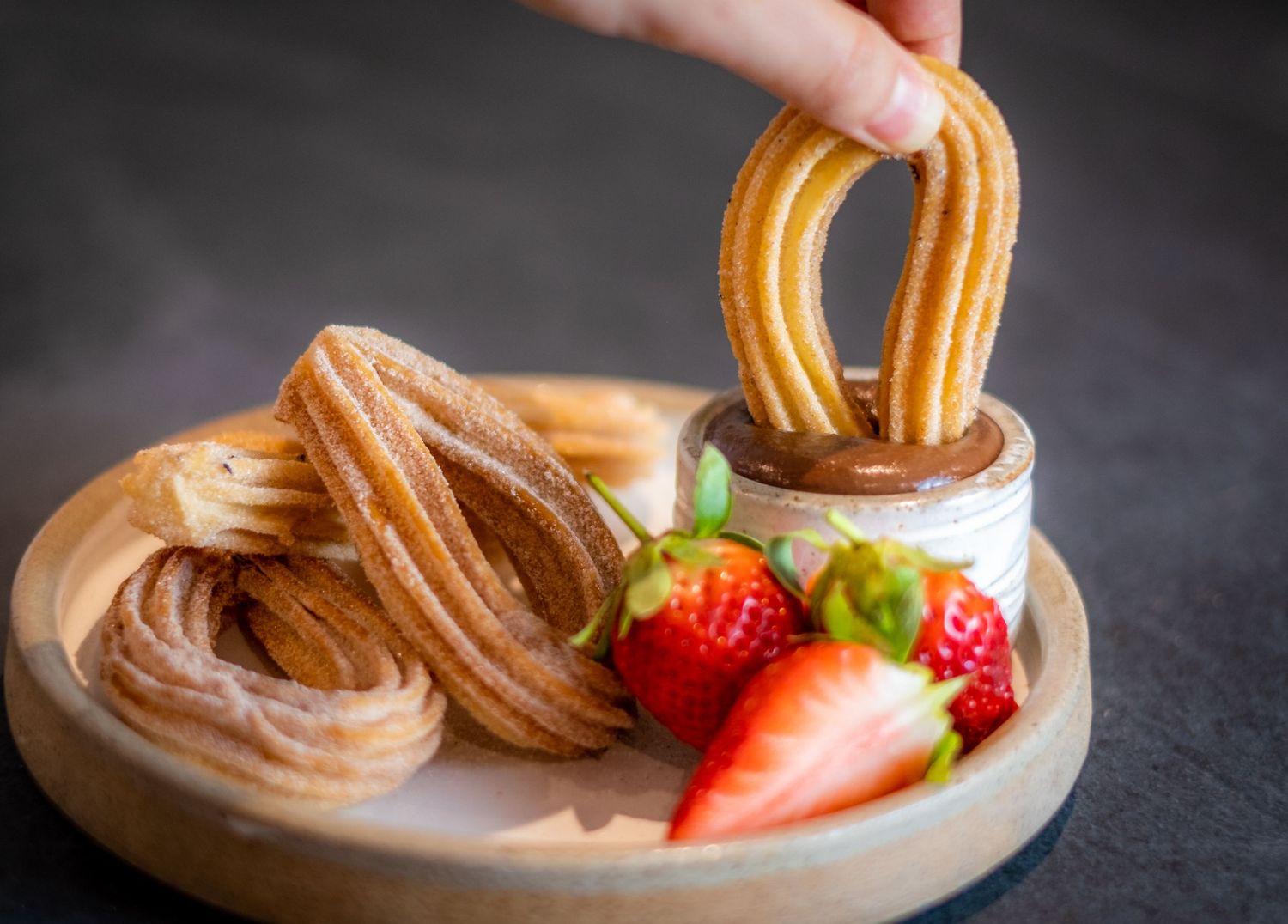 A studio shot of a delicious chocolate dessert showing someone dipping a churros into the chocolate