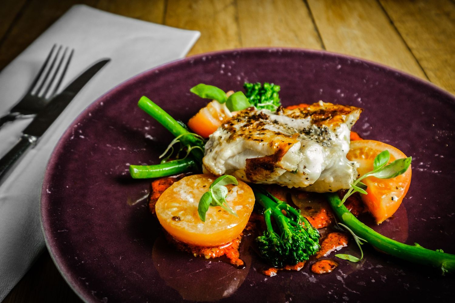 Close-up of beautifully cooked piece of fish served with cooked vegetables and tomatoes