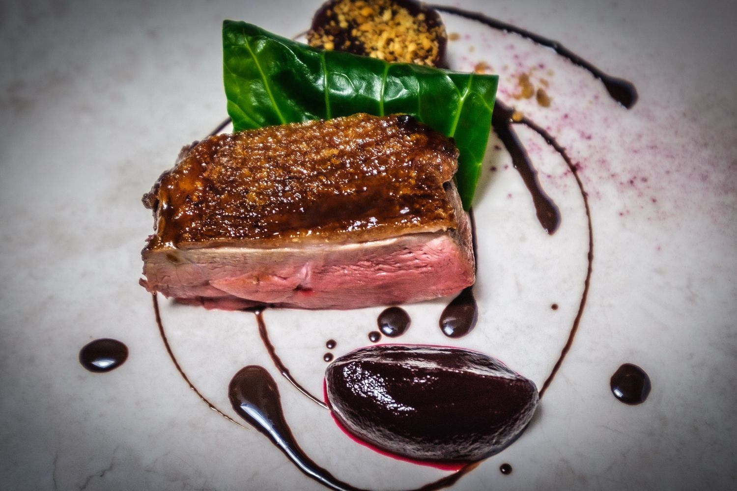 Seared meat with a pink center green vegetables and dark sauce on a pale plate, photographed by Simon Robertson.