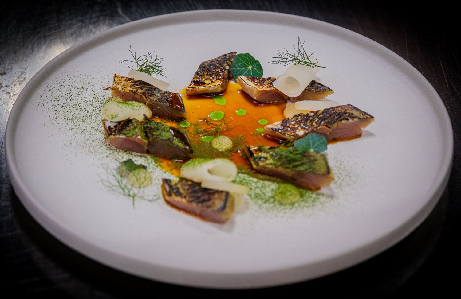Restaurant dish of smoked fish with orange purée, green vegetables and garnishes on a white plate, photographed by Simon Robertson.