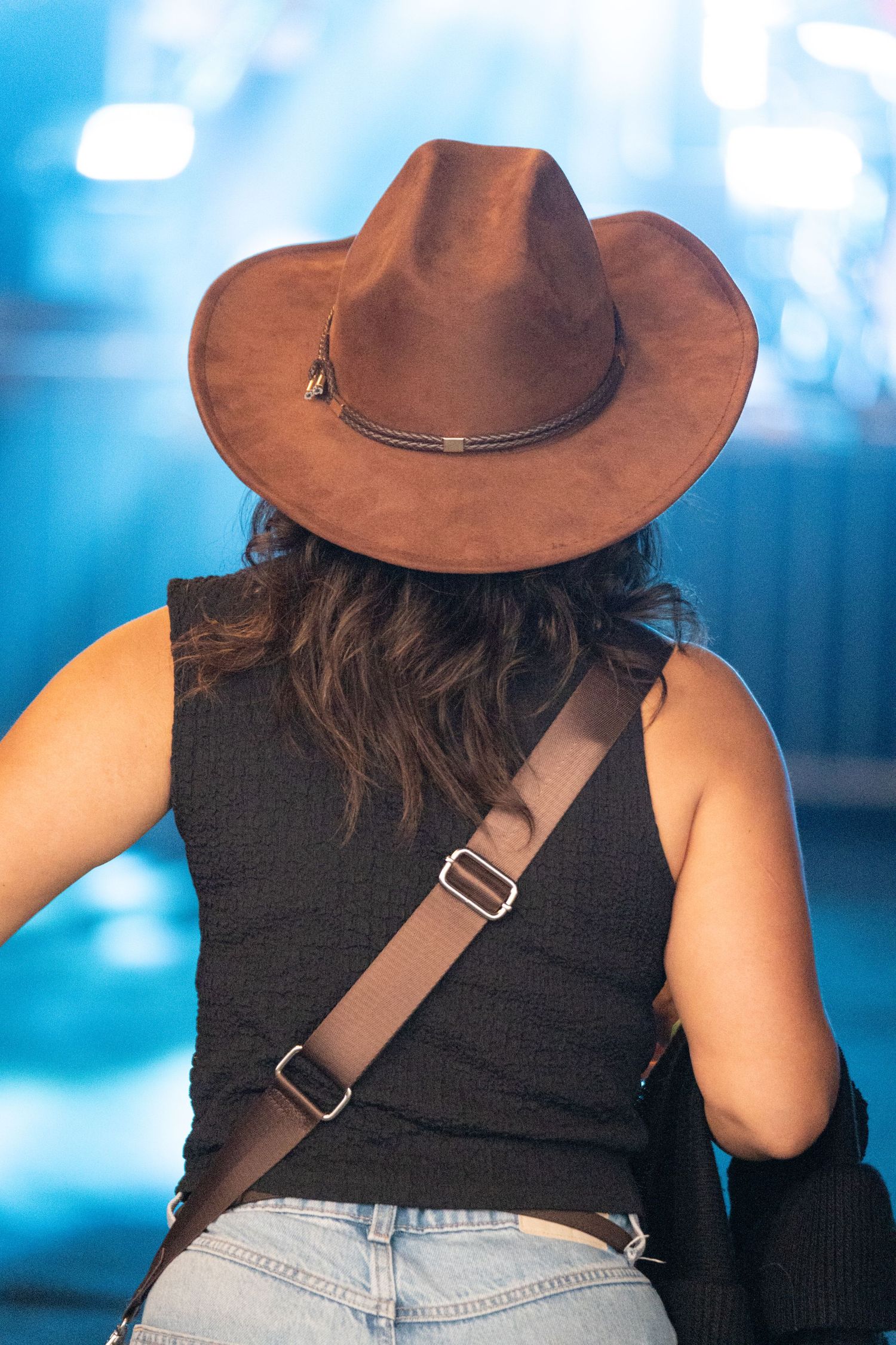 Festival attendee wearing a brown cowboy hat, viewed from behind against blue stage lighting, by Simon Robertson.