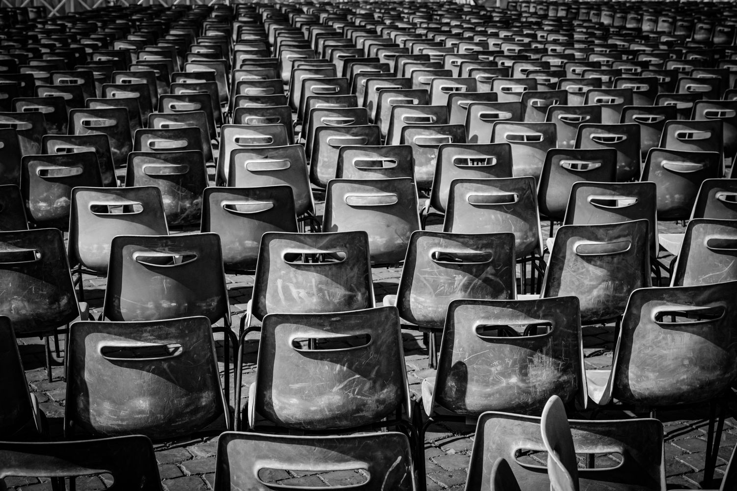 Black and white photograph of rows of empty chairs, with one chair facing the opposite direction, by Simon Robertson.