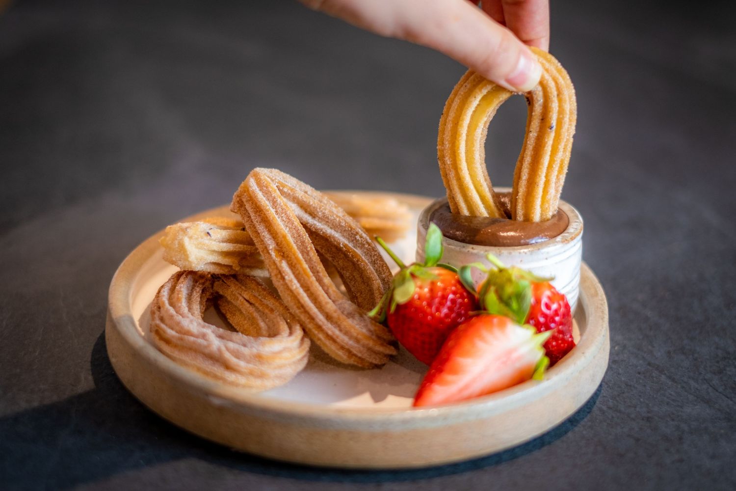 A studio shot of a delicious chocolate dessert showing someone dipping a churros into the chocolate