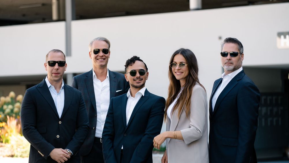 Five colleagues in business attire photographed together outside an office