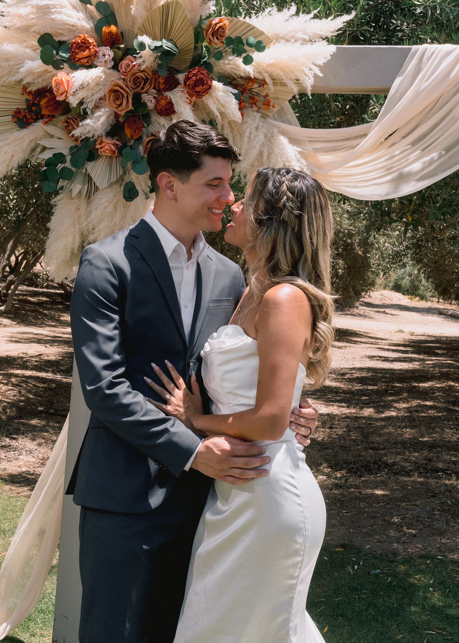 Bride and groom sharing first kiss at outdoor boho wedding ceremony with pampas grass decor.