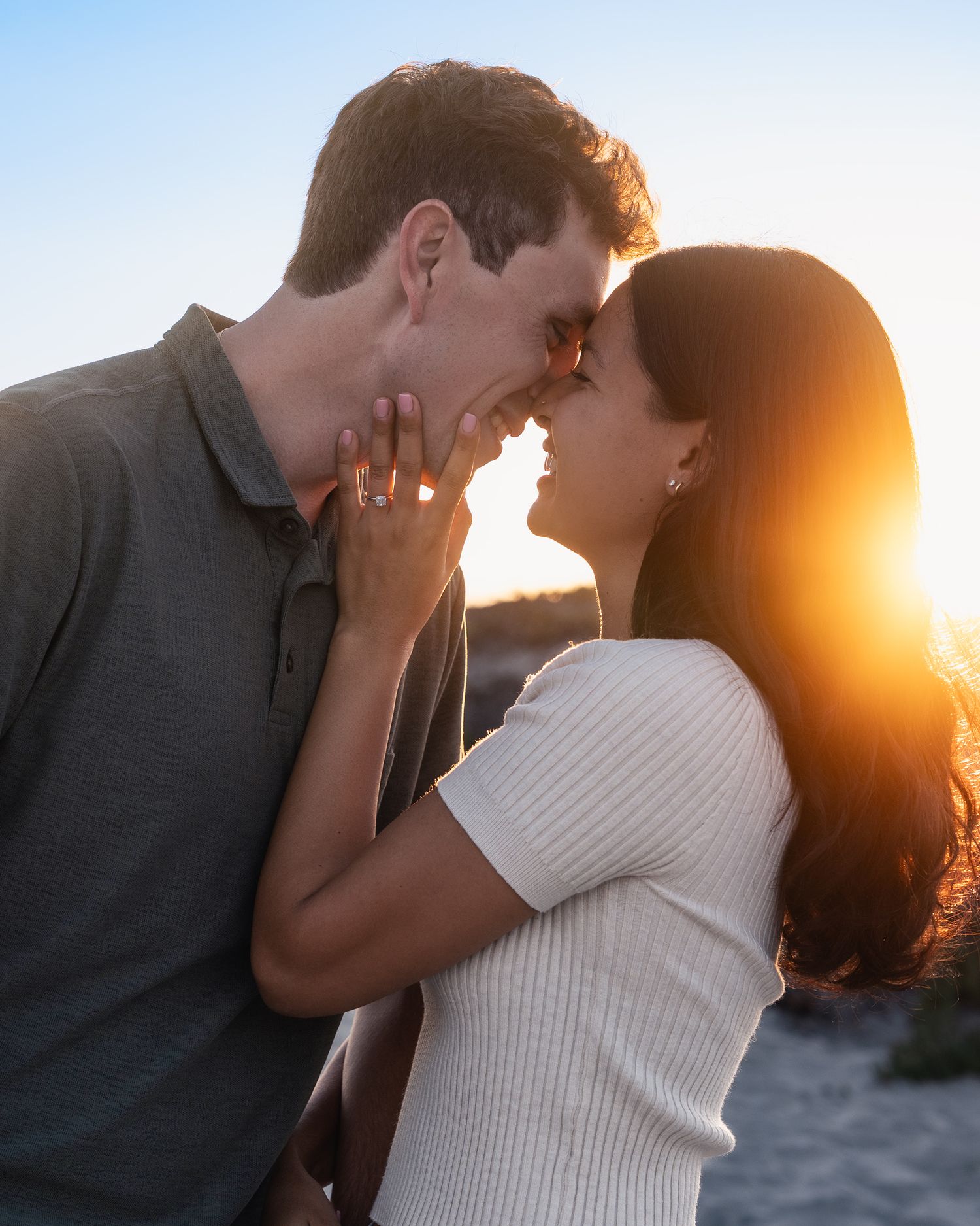 Couple nearly kissing with golden sunset glowing behind them on a romantic outdoor engagement session.