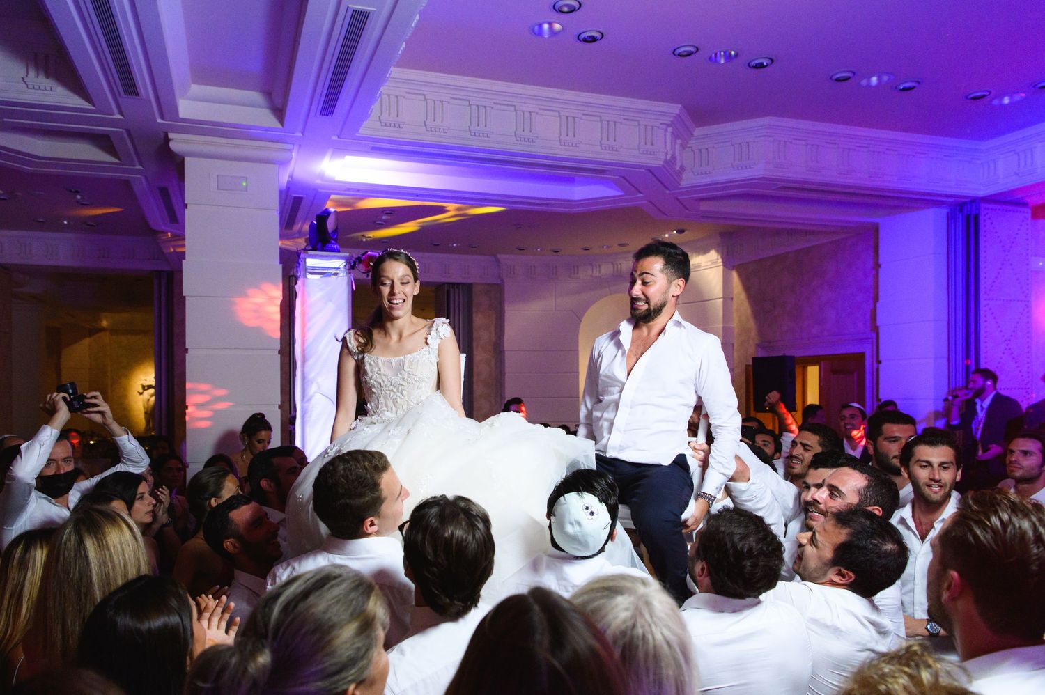 Bride and groom are lifted on chairs by cheering guests as they celebrate during a lively wedding reception dance.