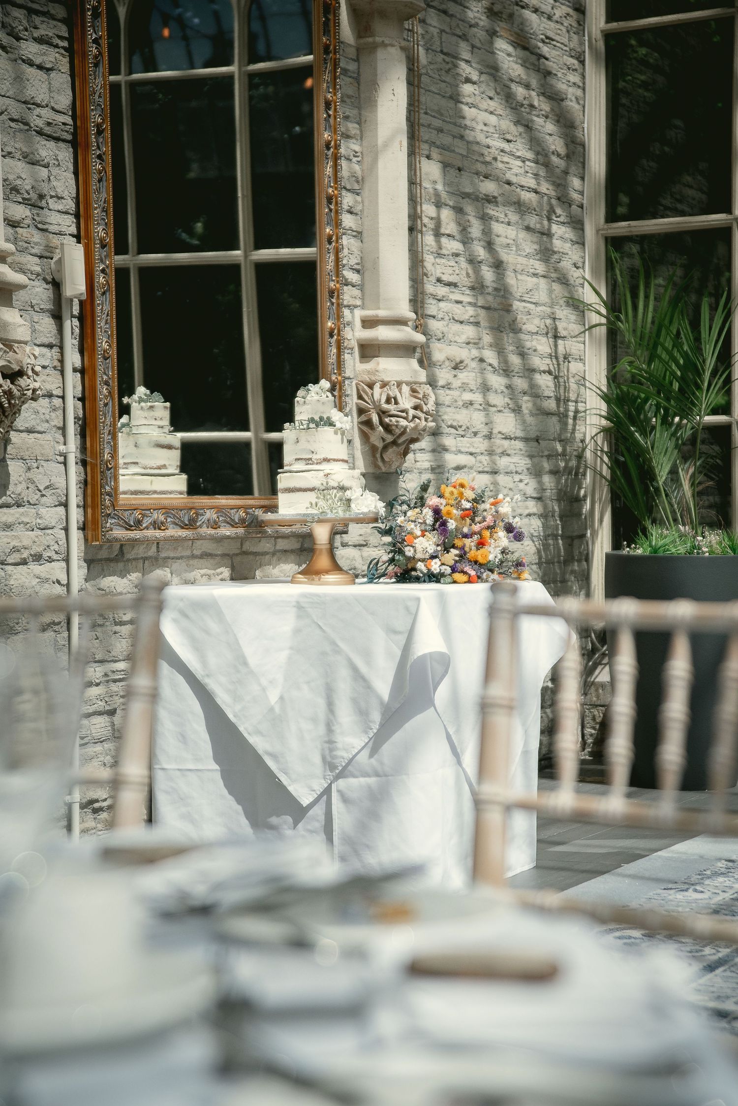 A wedding cake and floral arrangement displayed near a sunlit window with elegant table settings.