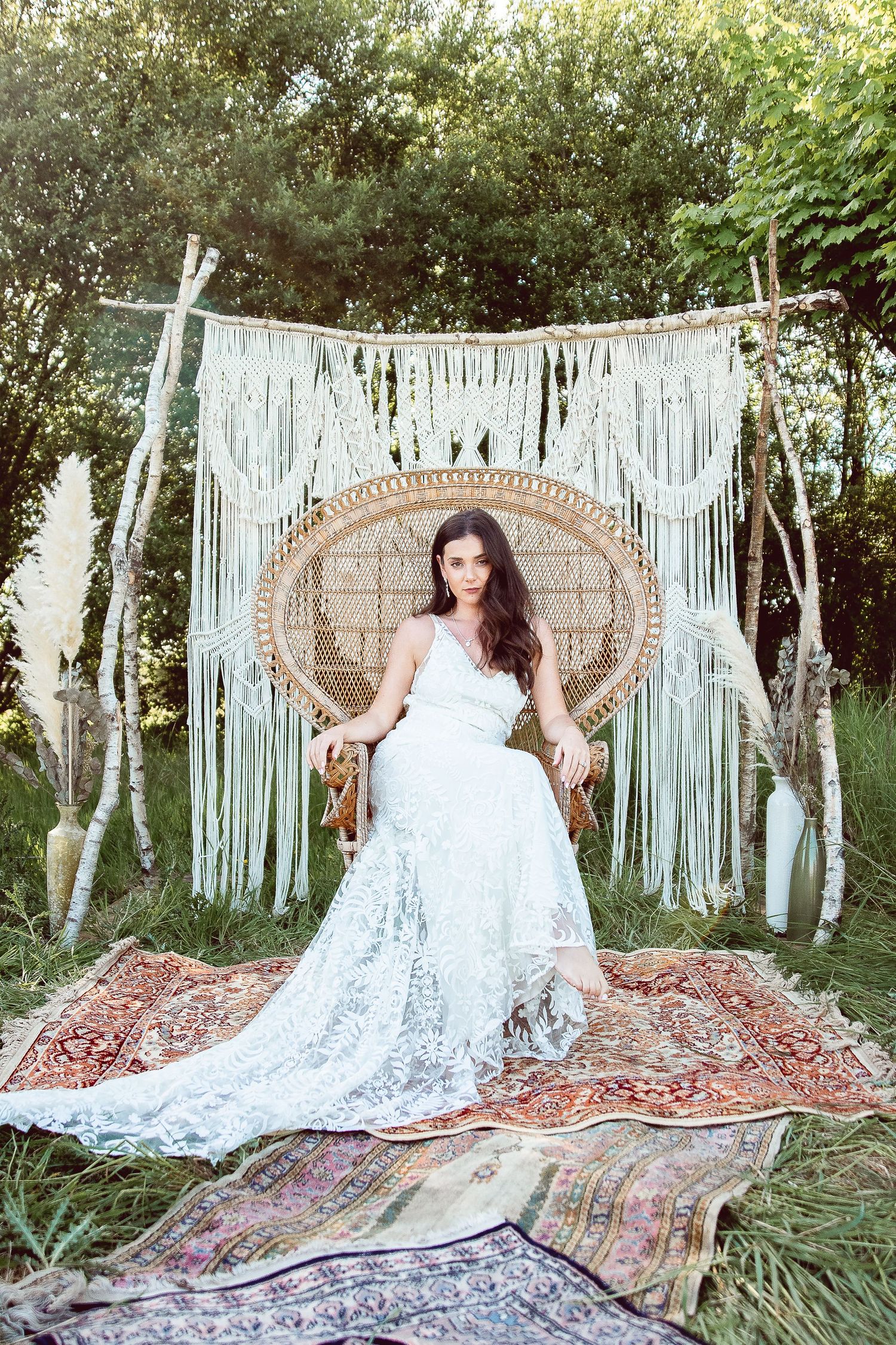 Boho bridal portrait on a peacock chair with layered rugs and macrame backdrop in a garden setting.