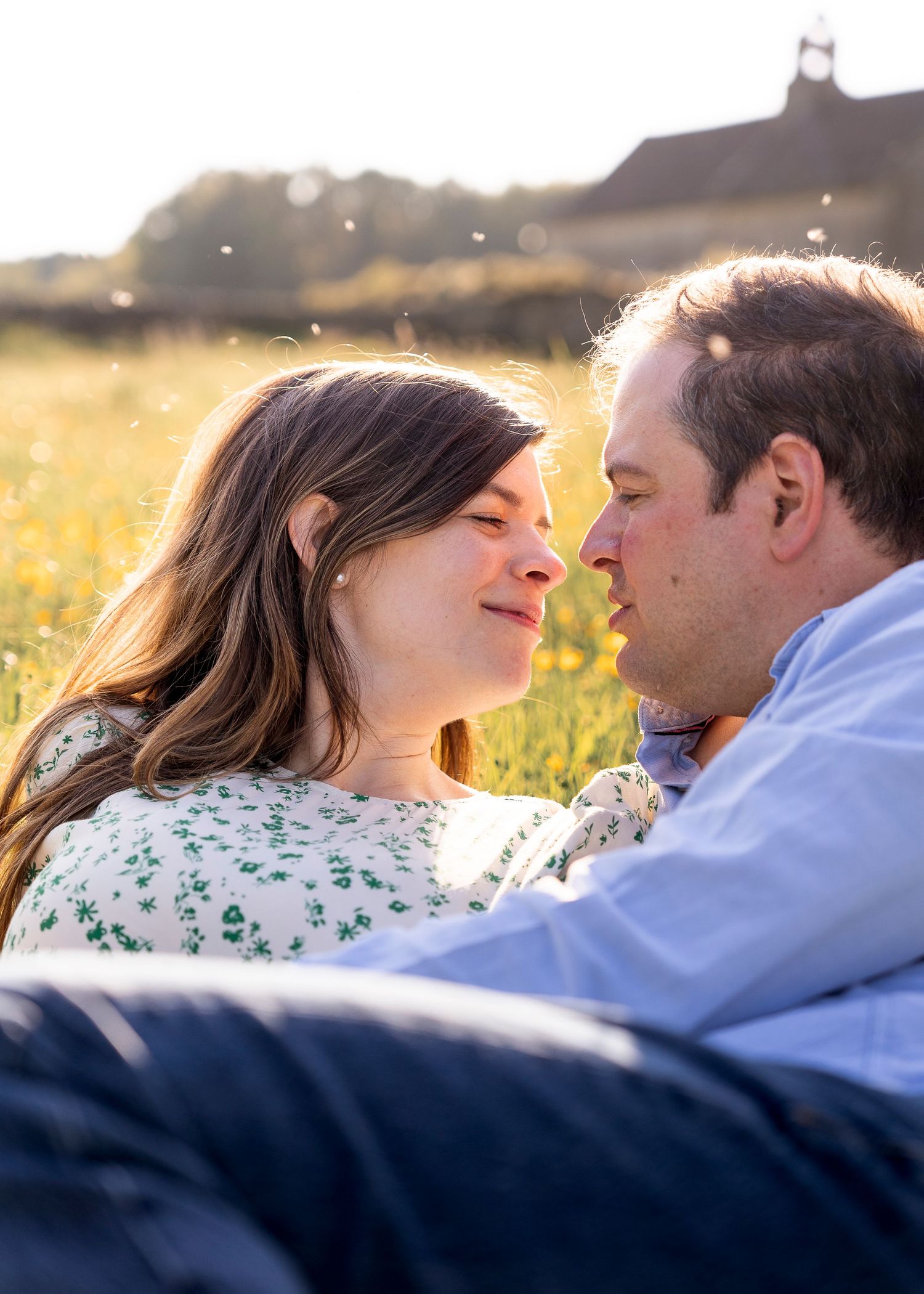 close up of couple about to kiss as they lie down in the middle of a buttercup field, sun shining behind them