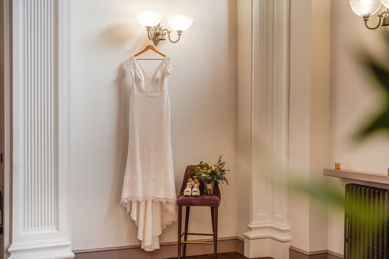 Dress hanging from wall light with shoes and bouquet placed on chair on the side