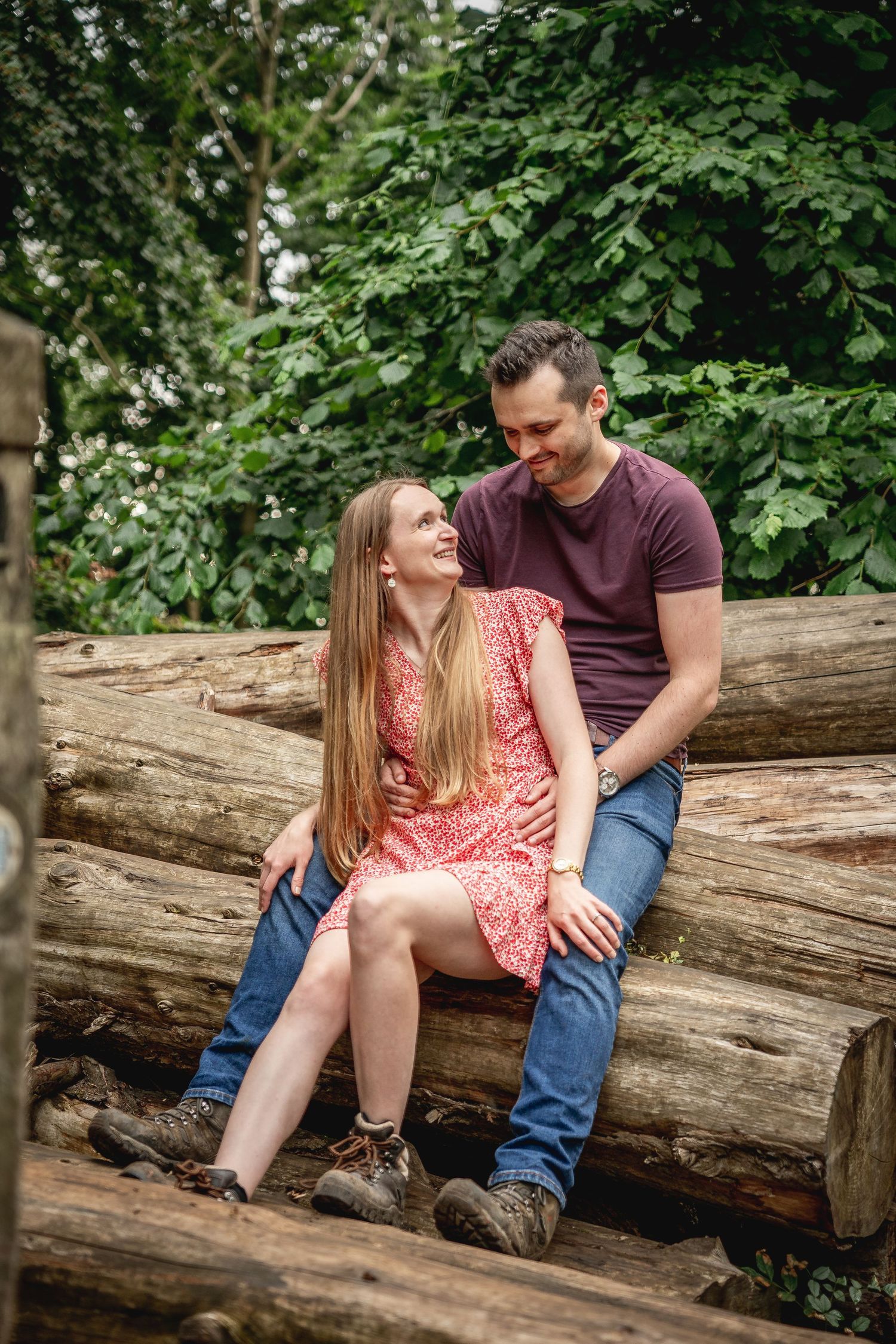couple sitting back to front on a pile of logs looking at each other, woman sat between mans' legs,