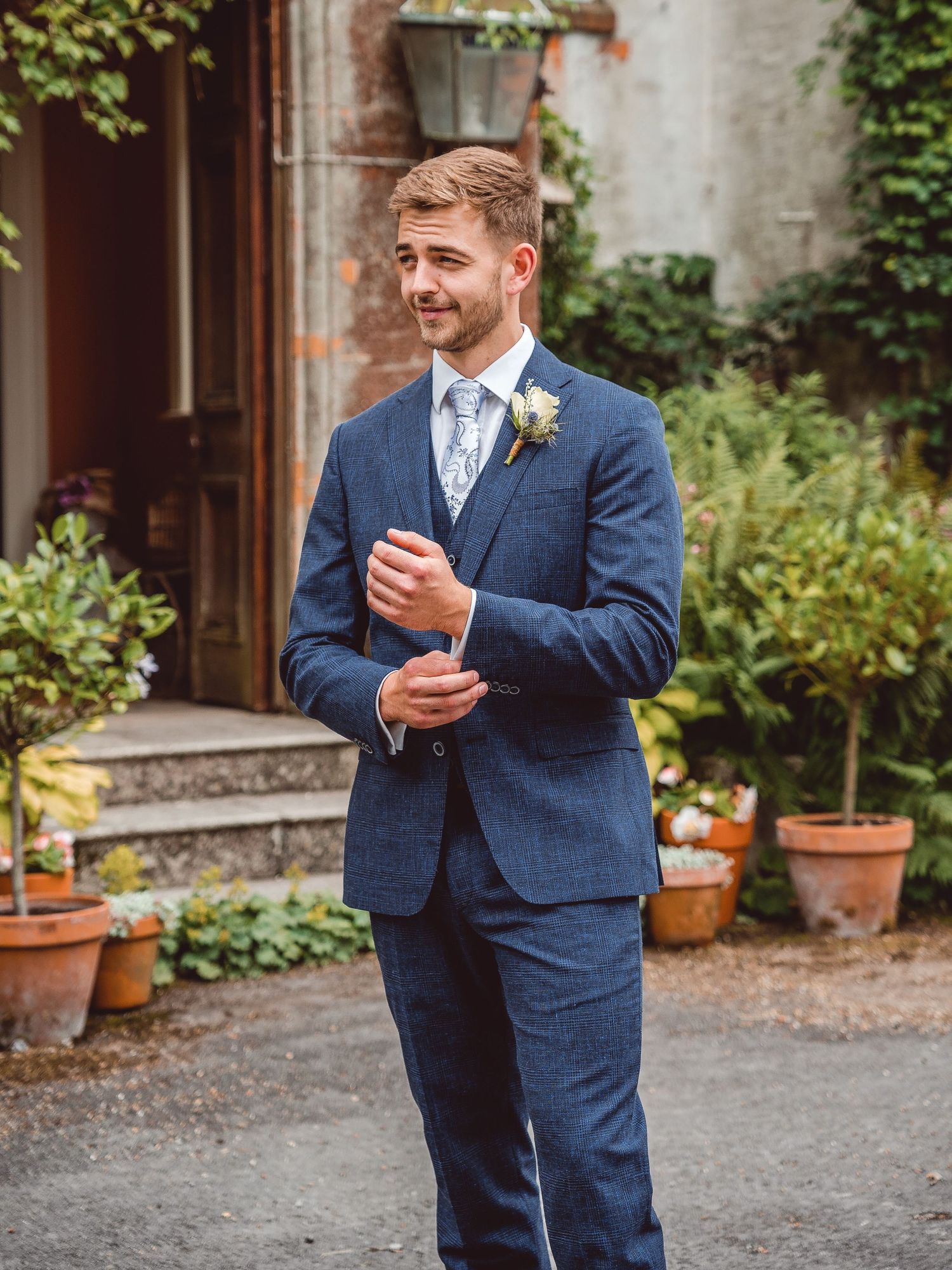 Groom portrait in blue tweed suit and light blue tie in front of the venue