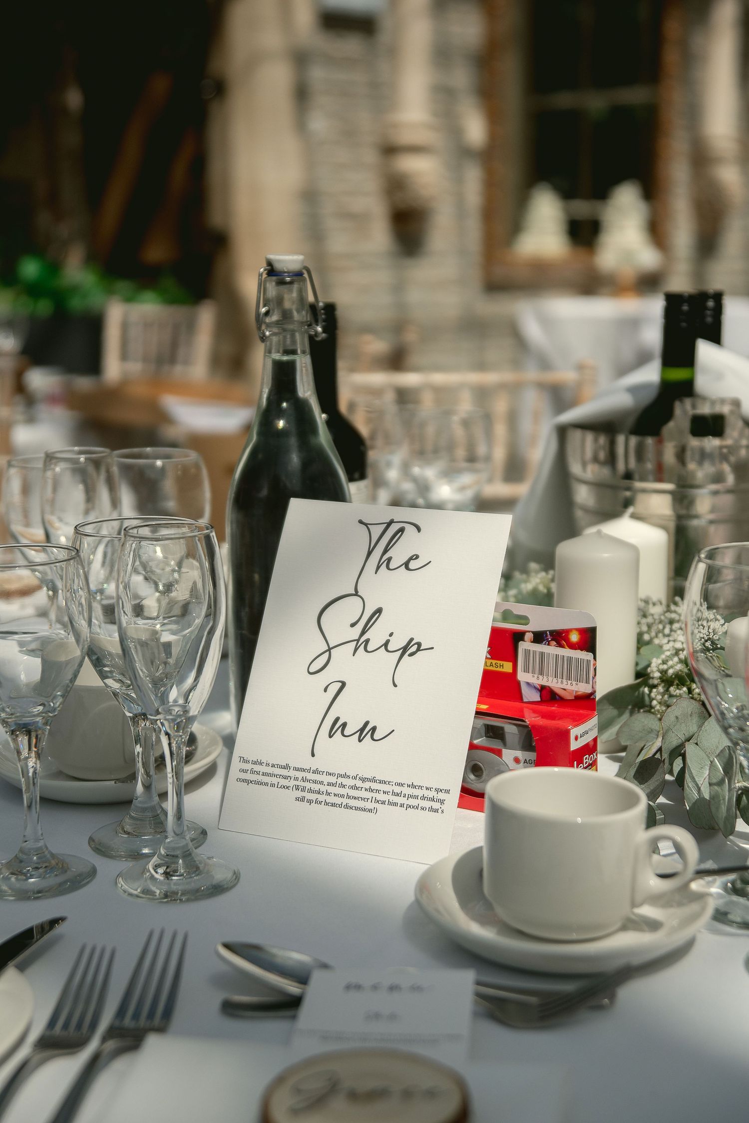An elegant wedding table setting with a 'The Ship Inn' sign, wine glasses, and delicate floral decorations.