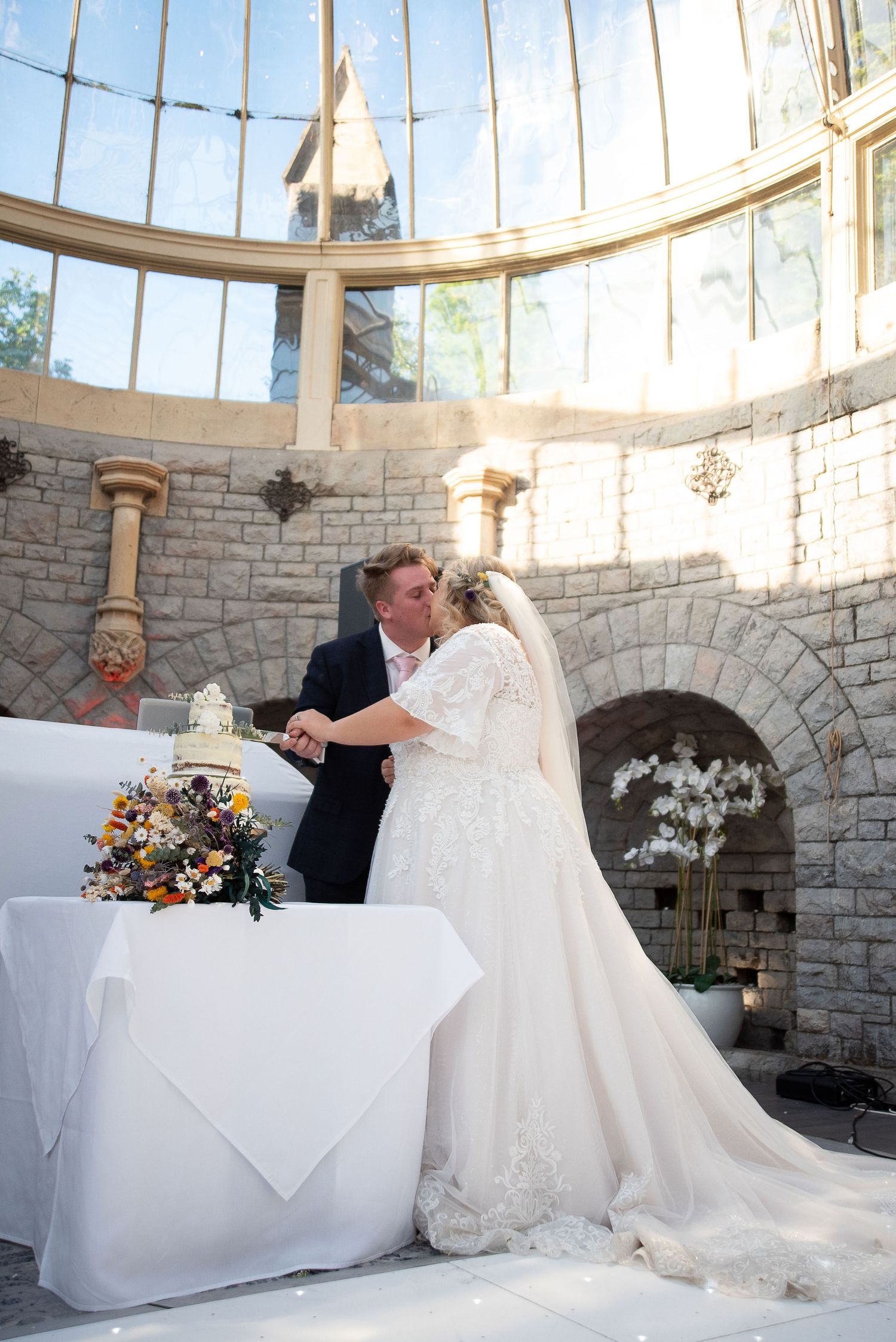 A wedding ceremony in a stunning glass-domed conservatory with stone walls and floral decorations.