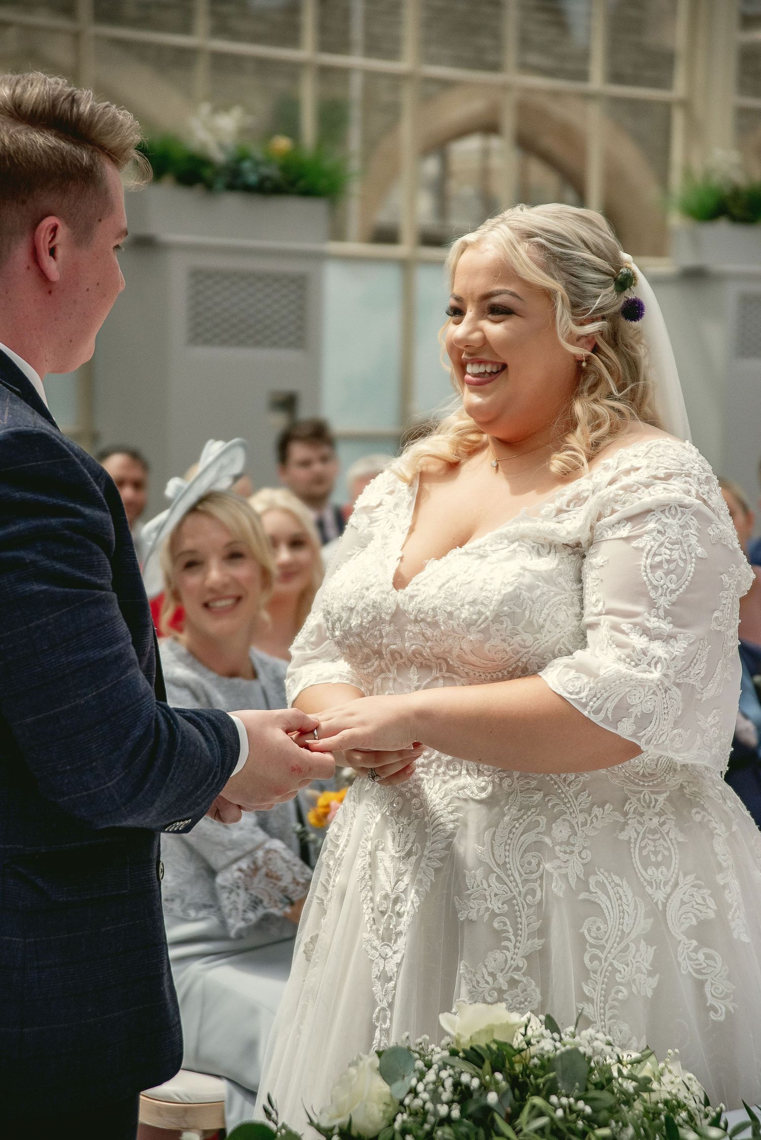 Joyful exchange of rings during wedding ceremony in an ornate indoor venue.