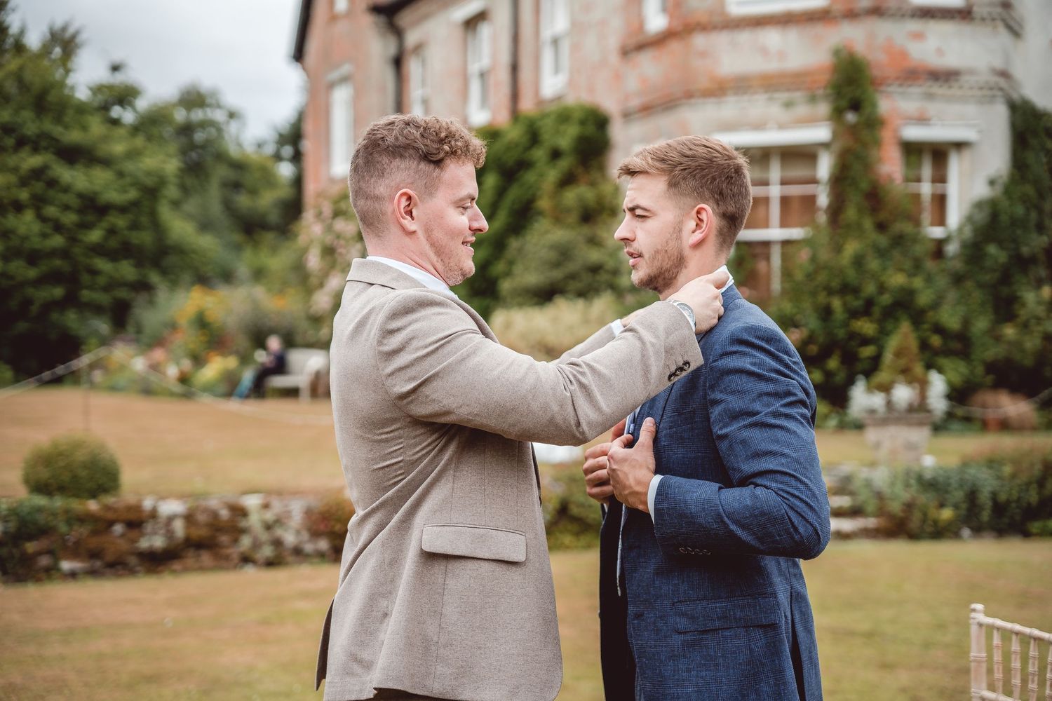 Candid shot of groomsman helping groom put on his tie in front of the venue