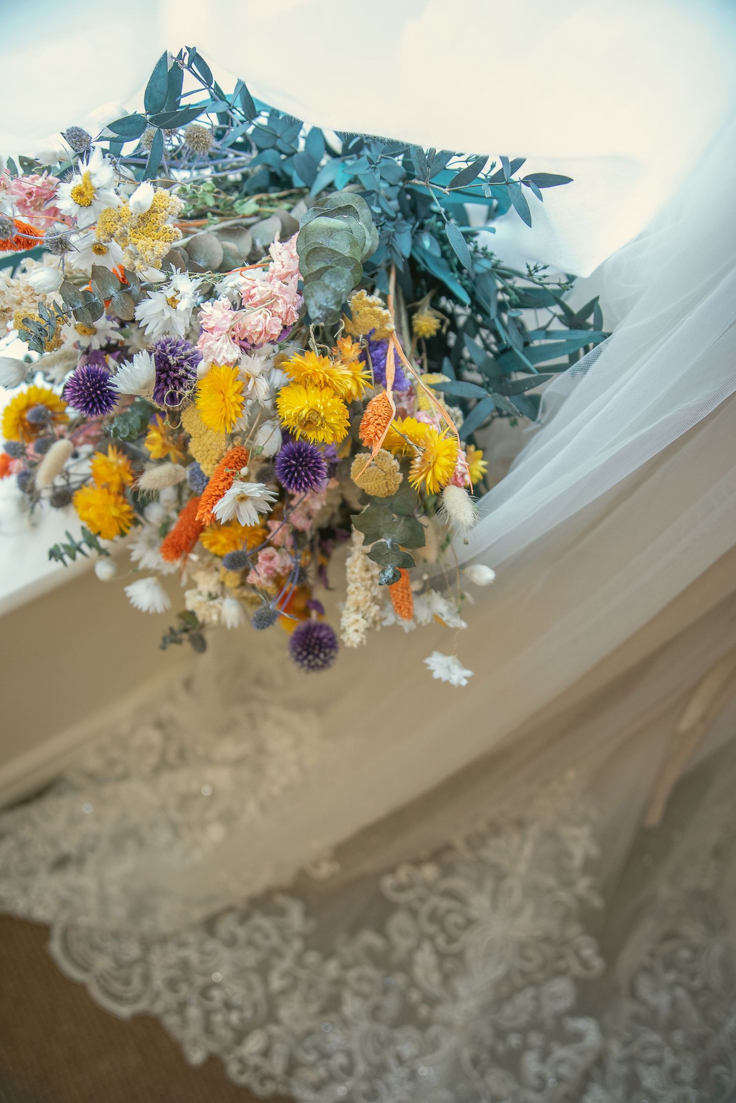 Colorful dried flowers and eucalyptus arranged with lace wedding dress details.