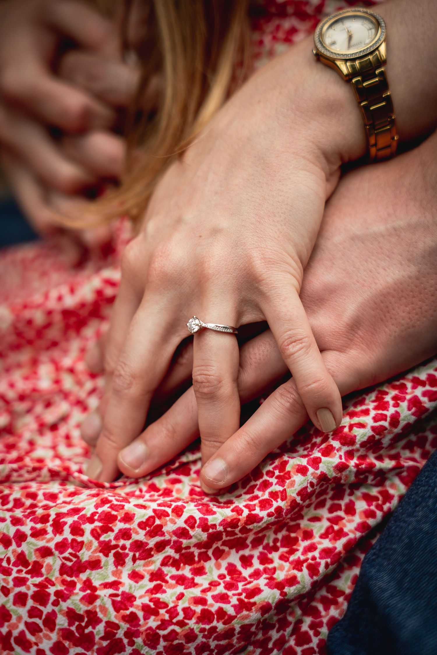 close up of hands intertwined and resting on her dress, top hand showing off the engagement ring
