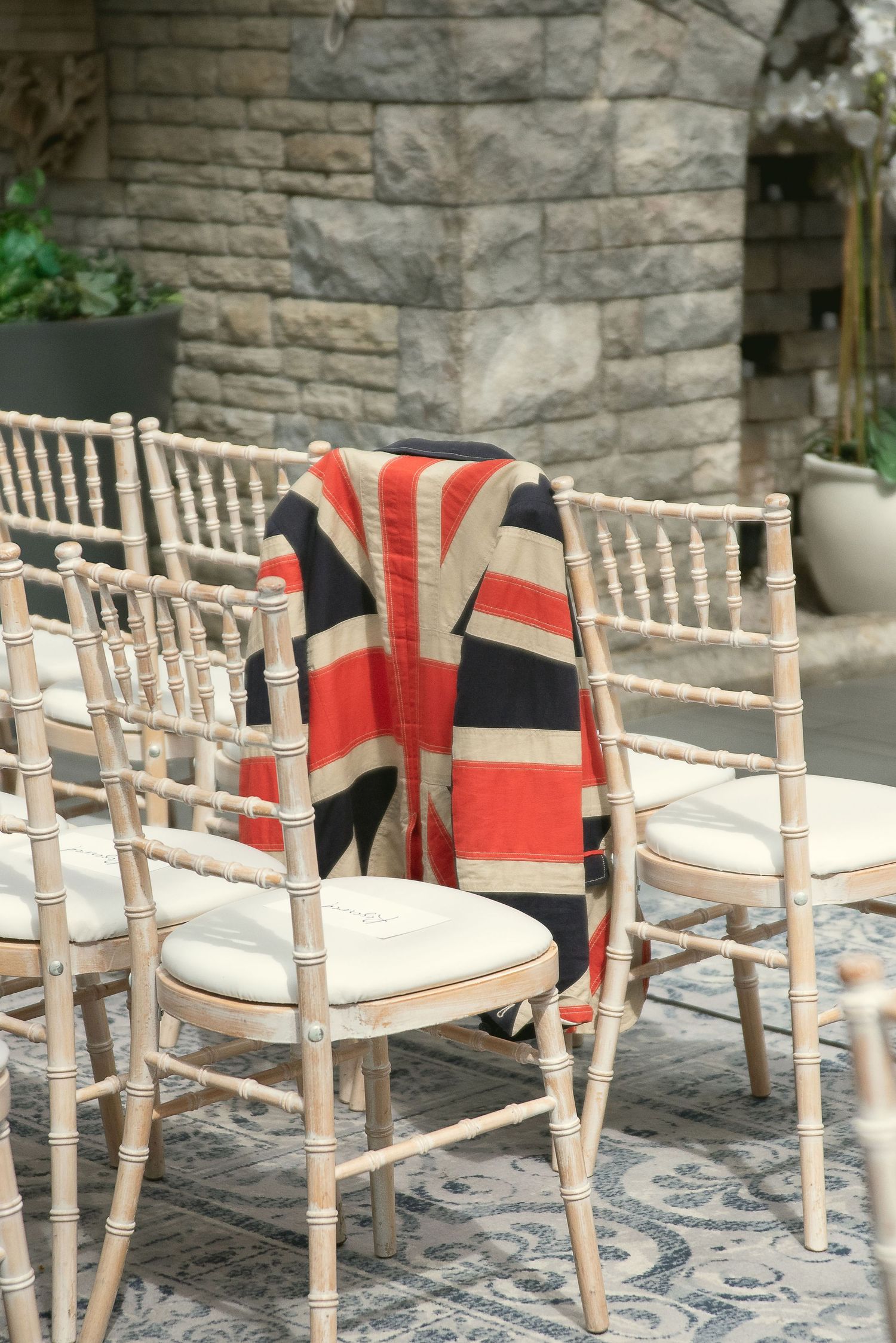 Light wooden chiavari chairs arranged for outdoor wedding ceremony with red blankets.