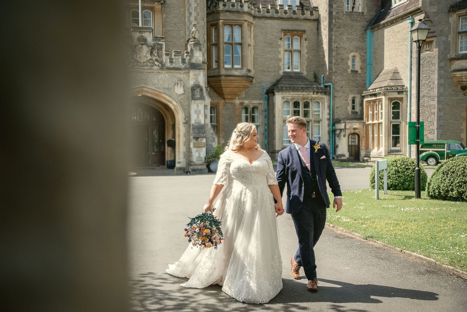 A wedding couple walks along a path outside a grand historic mansion on their special day.