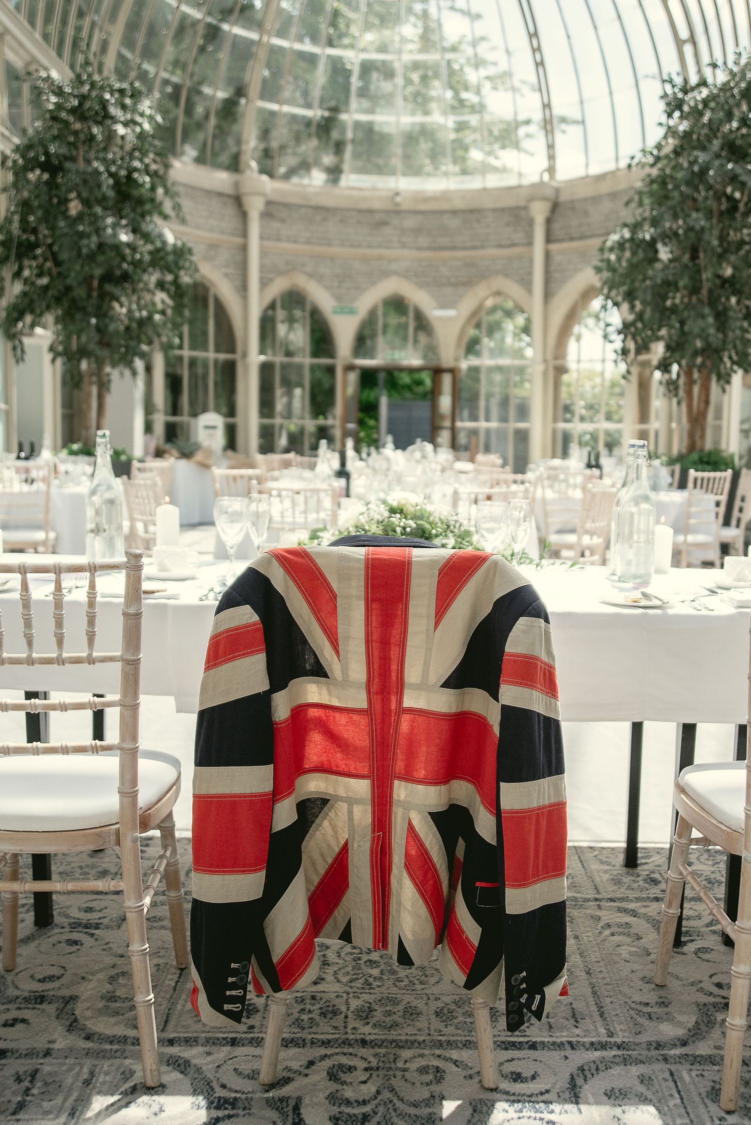 A Union Jack patterned jacket draped over a chair in a glass-domed conservatory wedding venue.