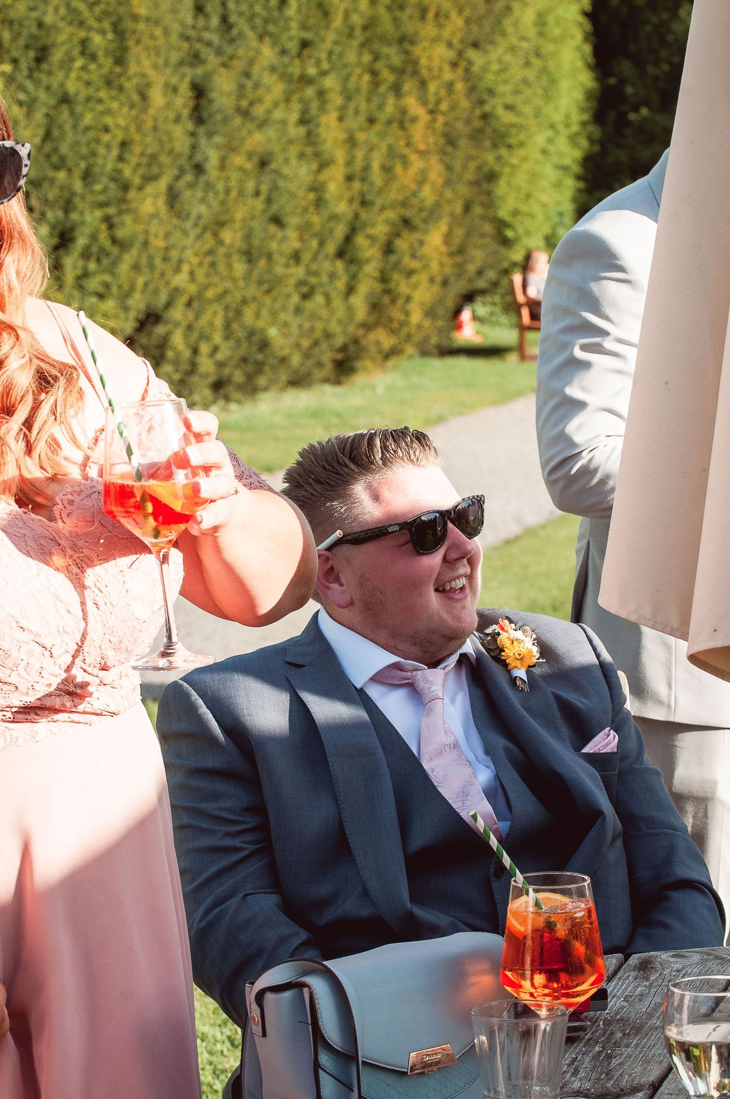 Wedding guests in formal attire enjoying drinks outdoors.
