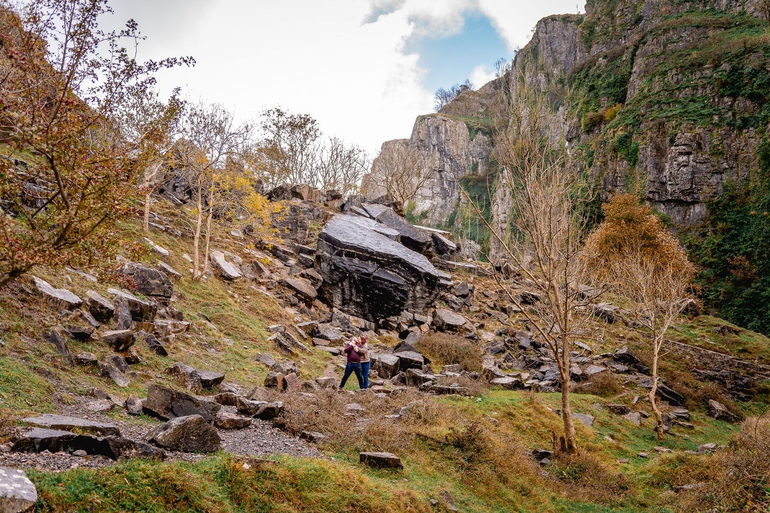 Landscape image or part of the gorge, boulders and logs litter the space, couple embracing in the distance in the middle of the scene