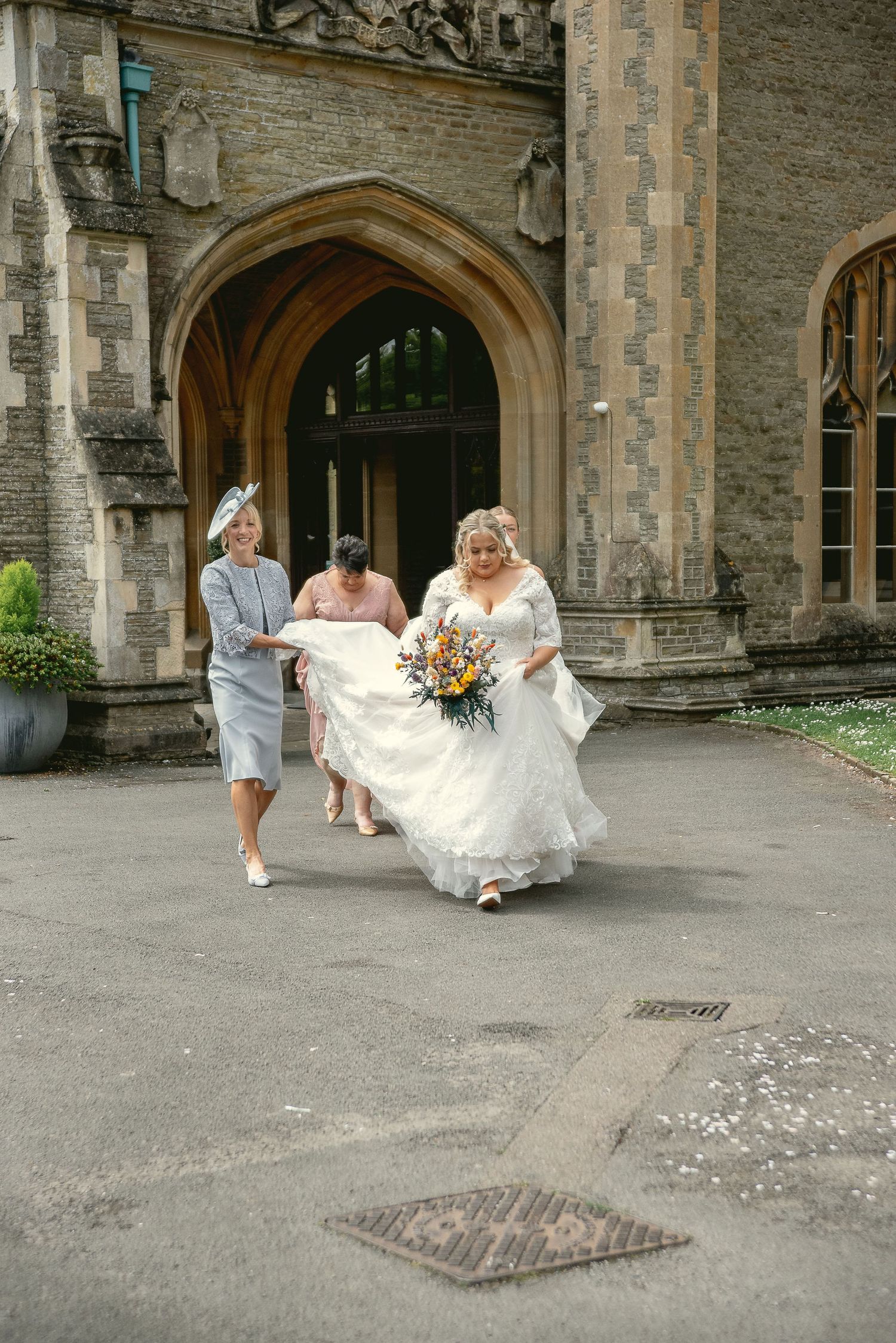 Wedding party helping with the bride's dress outside a gothic stone church entrance.