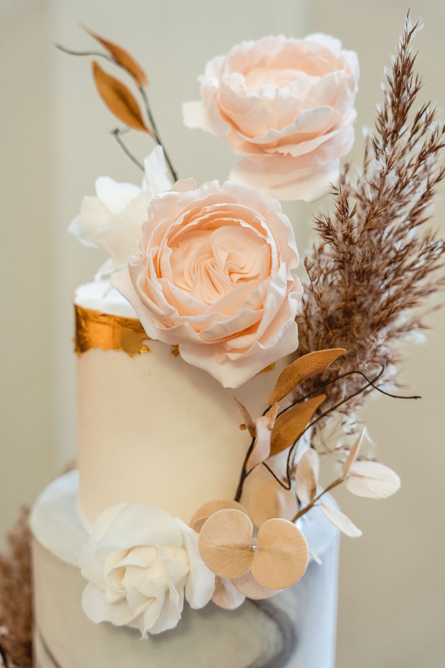 Details of cake decor - pink and white flowers, pampas grass and gold leaf detail