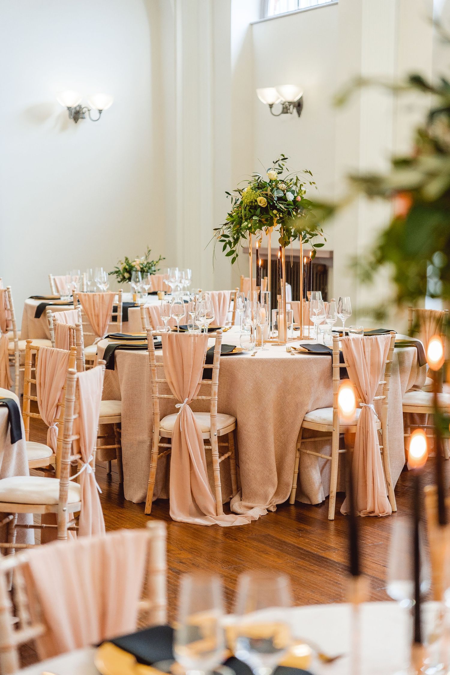 Close up of a table set up with pink chair sashes, pink table cloths and black and gold table decor