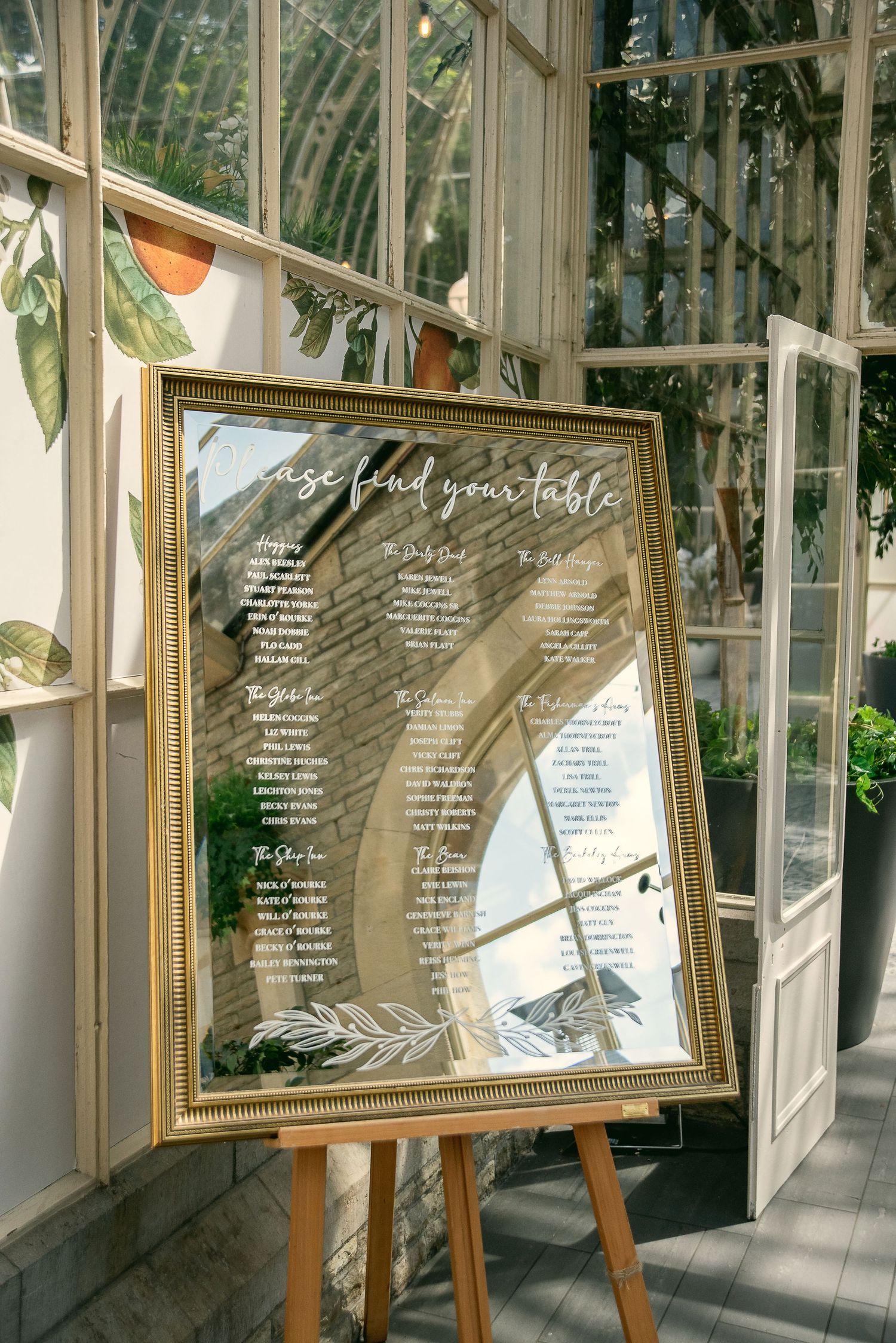 Elegant framed seating charts displayed in a sunlit conservatory space.