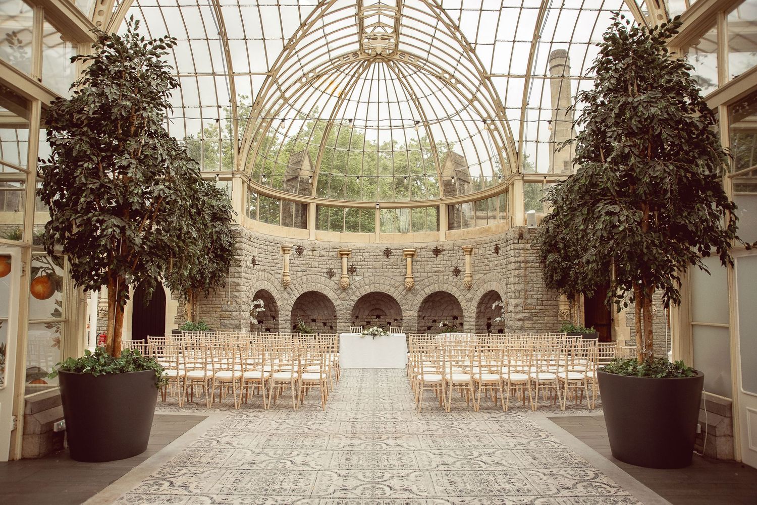 Elegant conservatory venue with arched glass ceiling and stone columns creates a bright, airy wedding ceremony space.