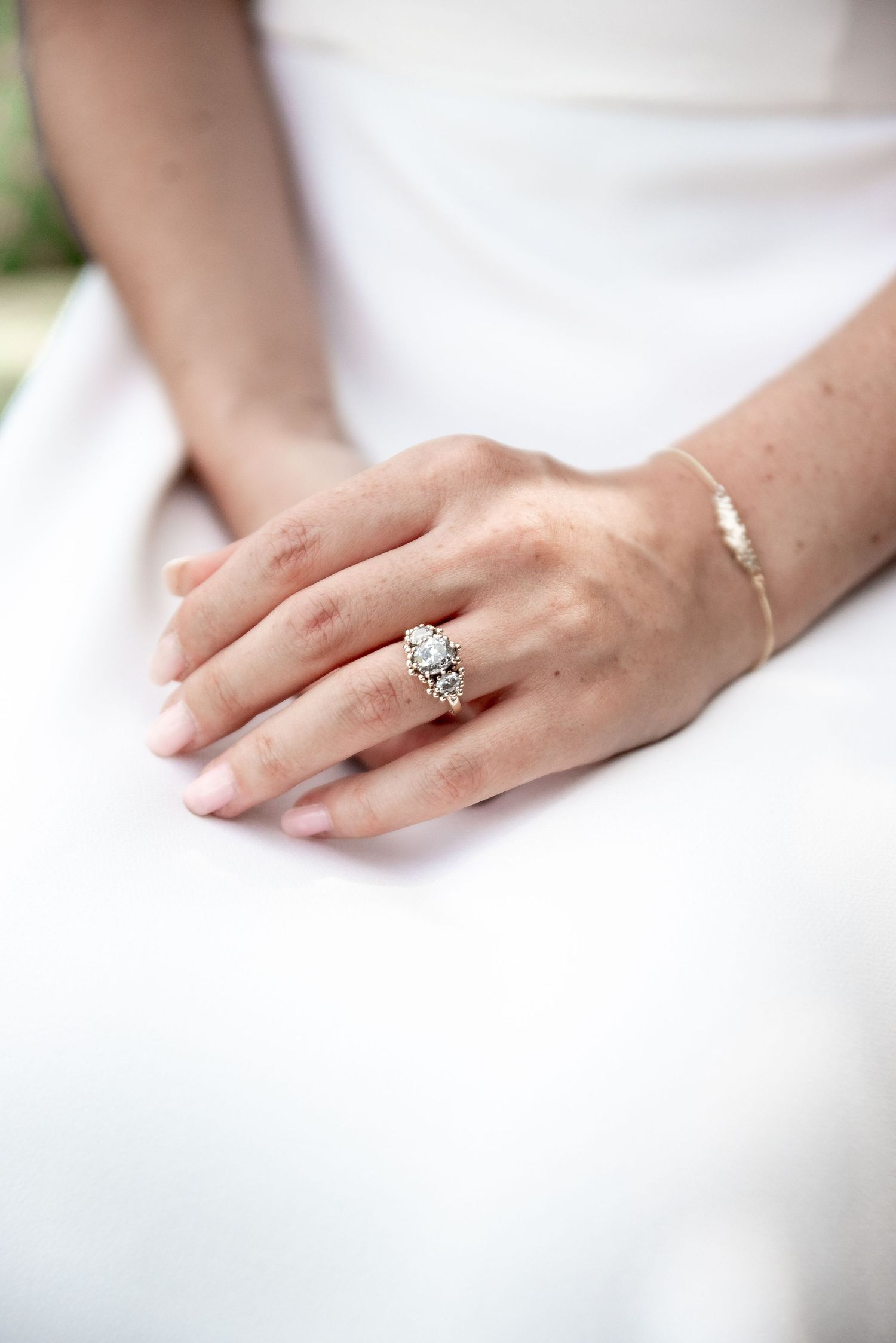 Close-up of hands wearing an elegant engagement ring against white fabric.