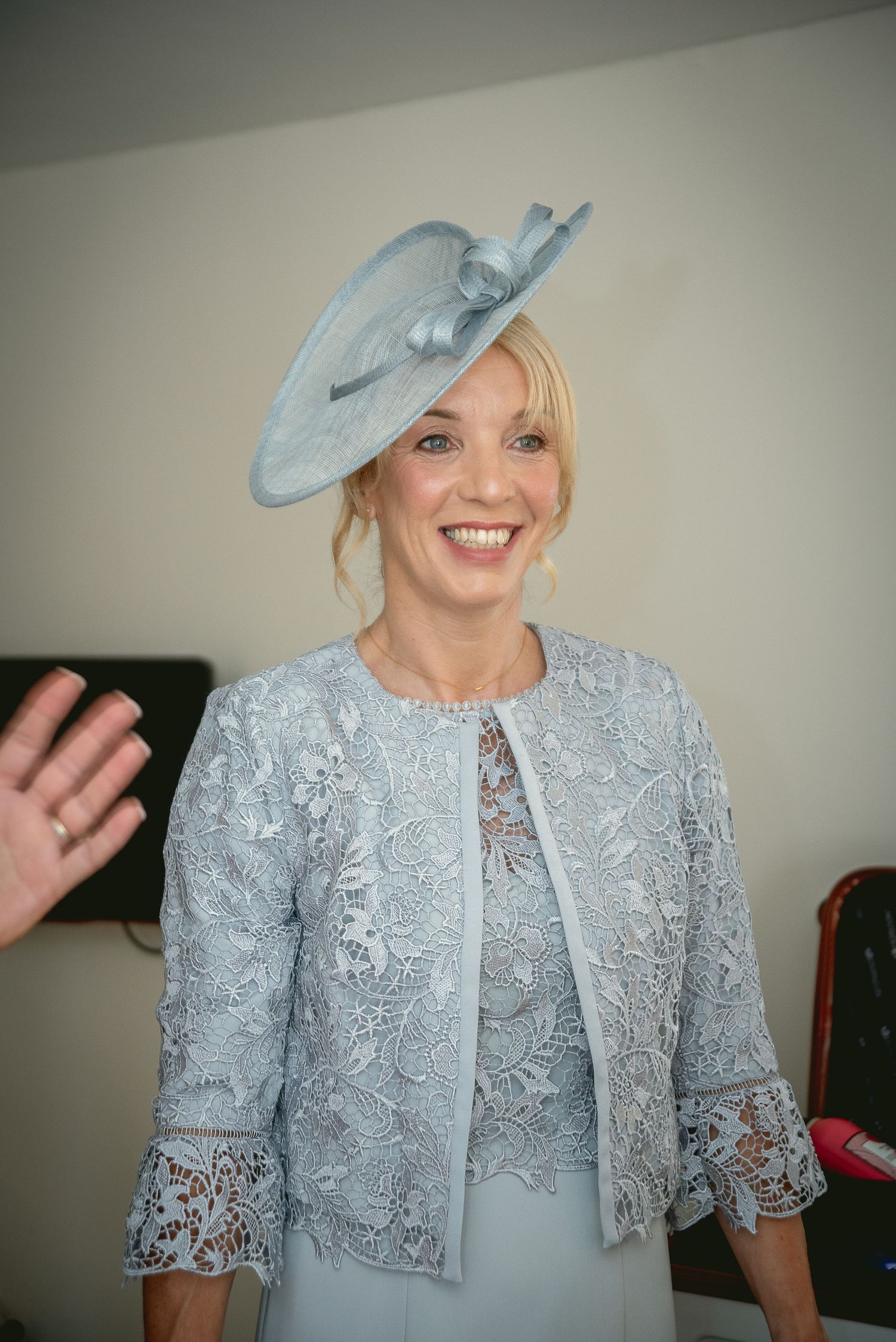 Elegant woman wearing a pale blue lace jacket and matching fascinator hat at a formal event.