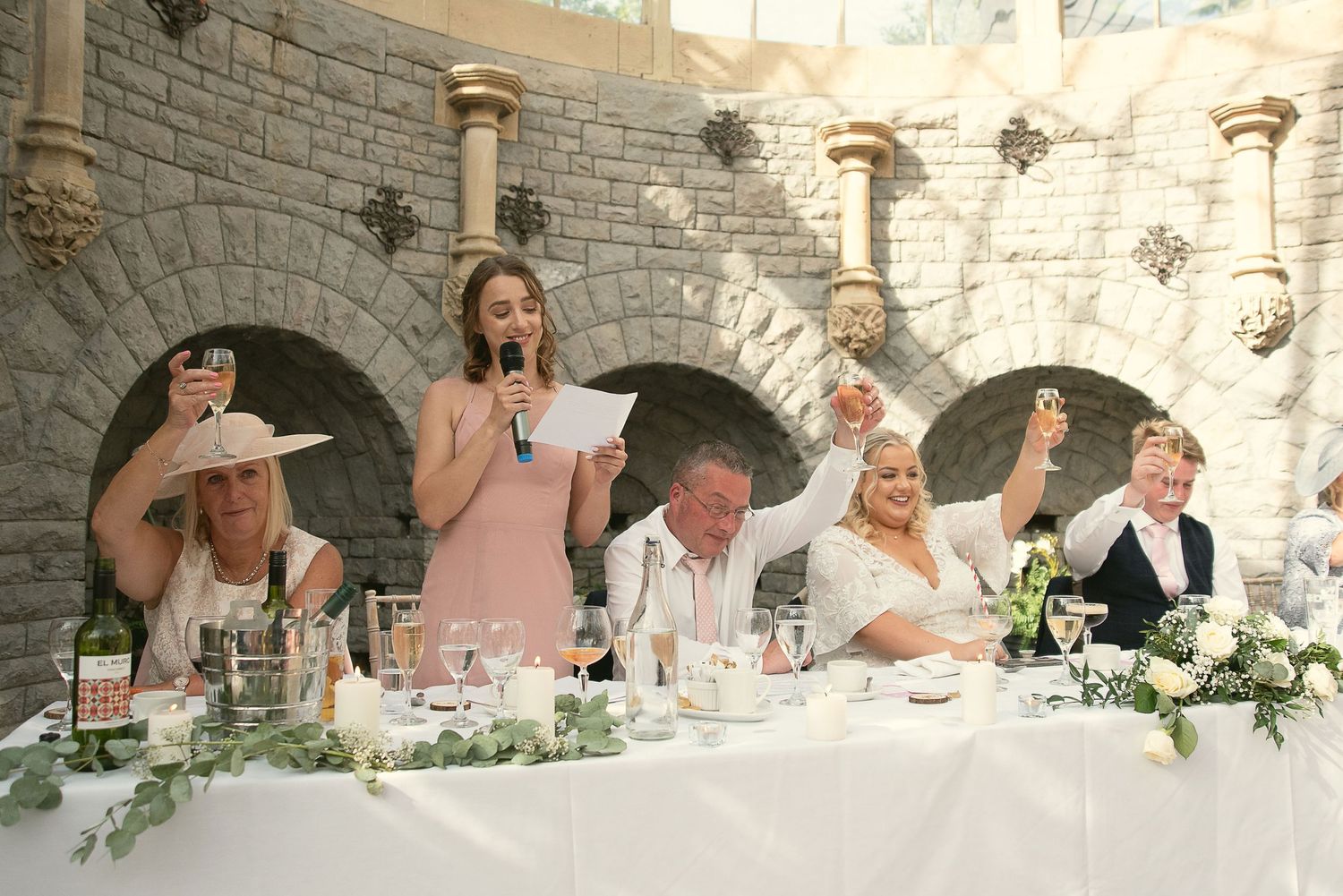 Wedding guests seated at stone archway venue share laughter and conversation during reception dinner.